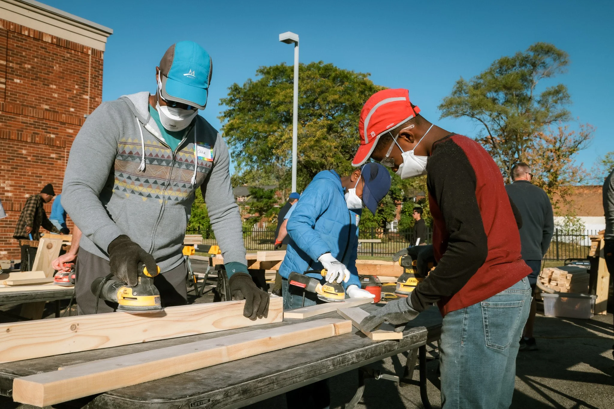 People building a wooden project outdoors while wearing masks and gloves.