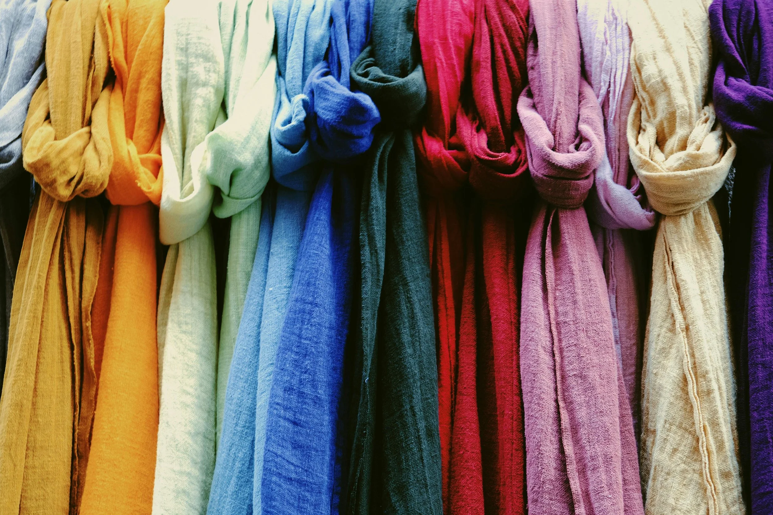 Colourful scarfs hanging in a rainbow order from orange to purple.