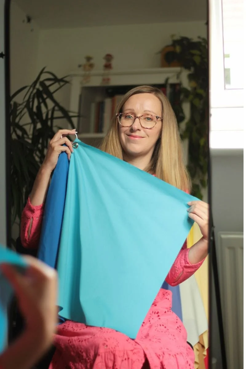 A picture of a woman looking in a mirror holding up a blue drape to her face