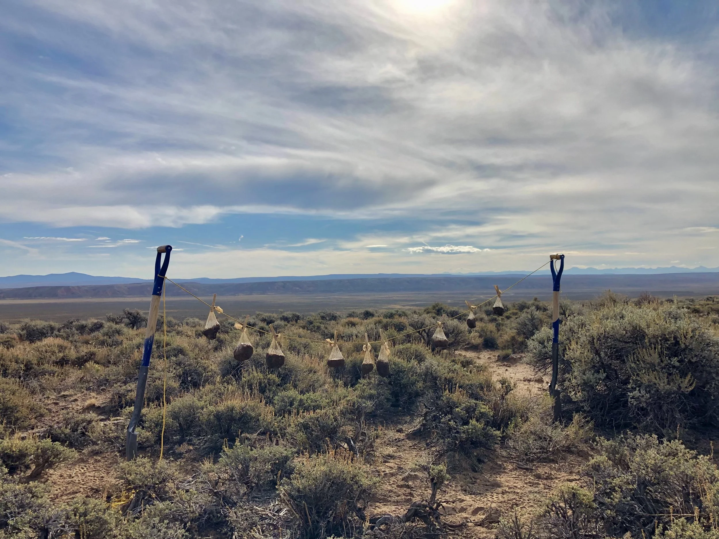 A landscape with a vast open sky filled with clouds, distant mountains, and a dry, shrub-covered plain in the foreground with outdoor gym equipment.