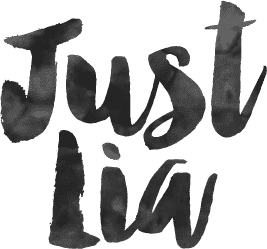 Logotipo escrito 'Just Lia' em estilo artístico com efeito de pincel ou aquarela, em tons de preto e cinza.