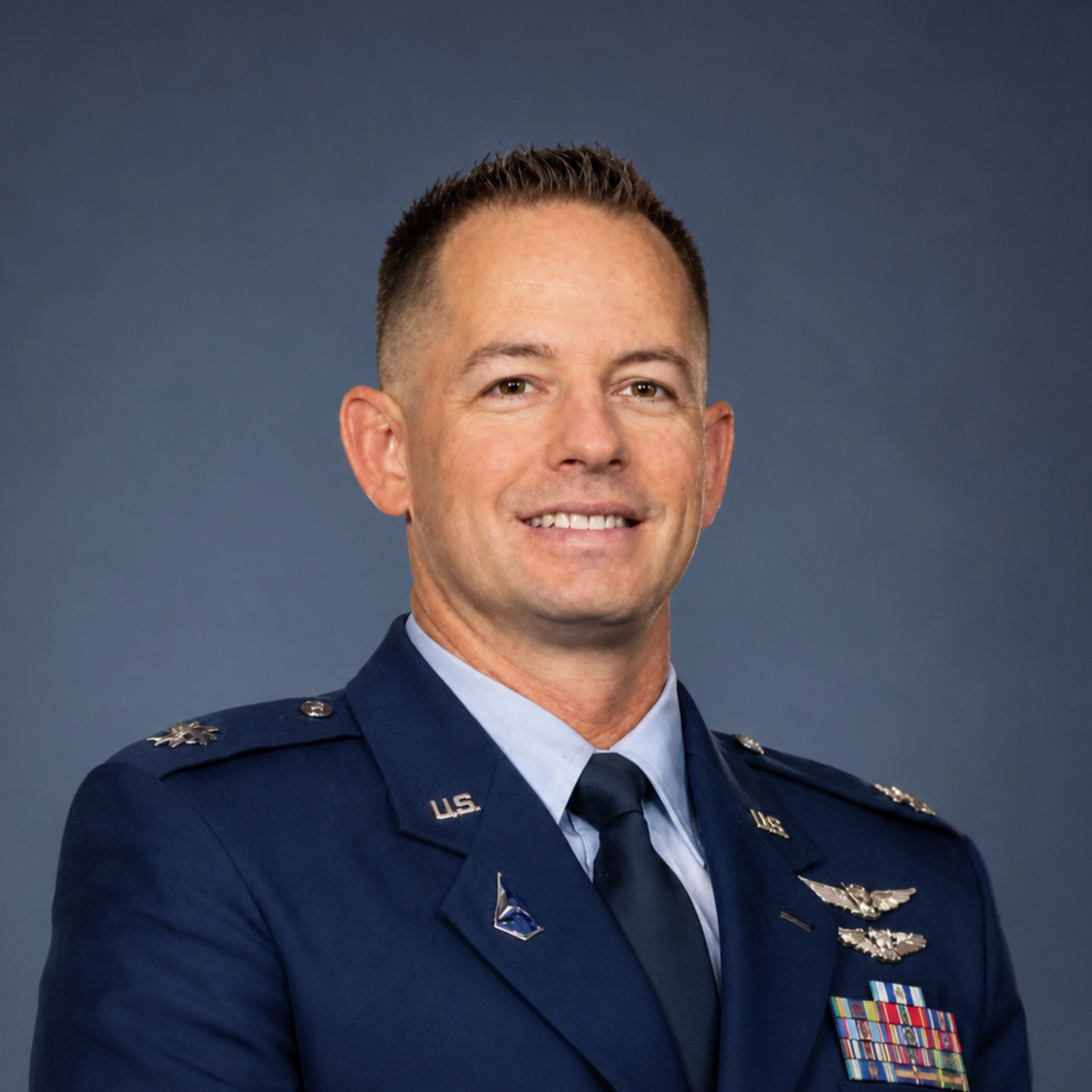 Portrait of a smiling male in U.S. Air Force uniform with medals and insignia, standing against a blue background.
