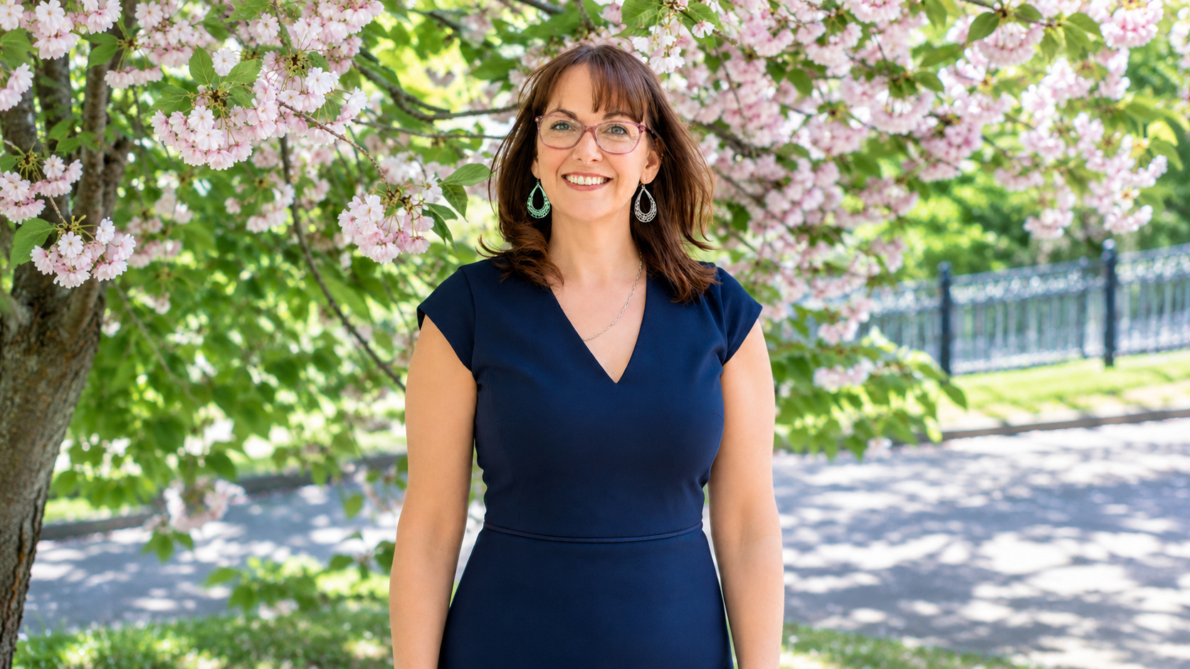 Cara Ugolini standing outdoors in front of a flowering tree with pink blossoms.