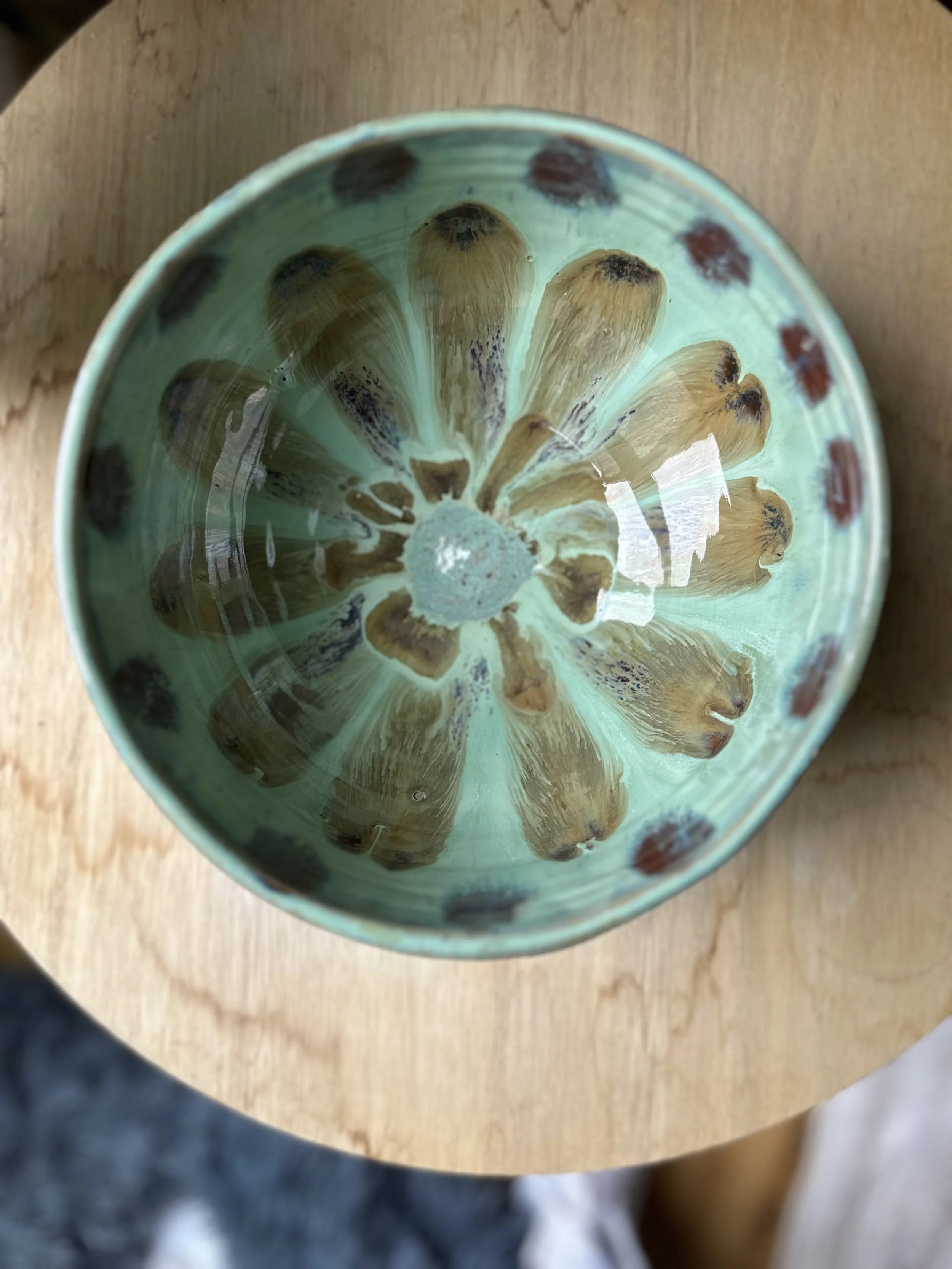 A ceramic bowl with a green interior and red and black polka dots, holding wooden spoons with rounded handles, placed on a wooden table.