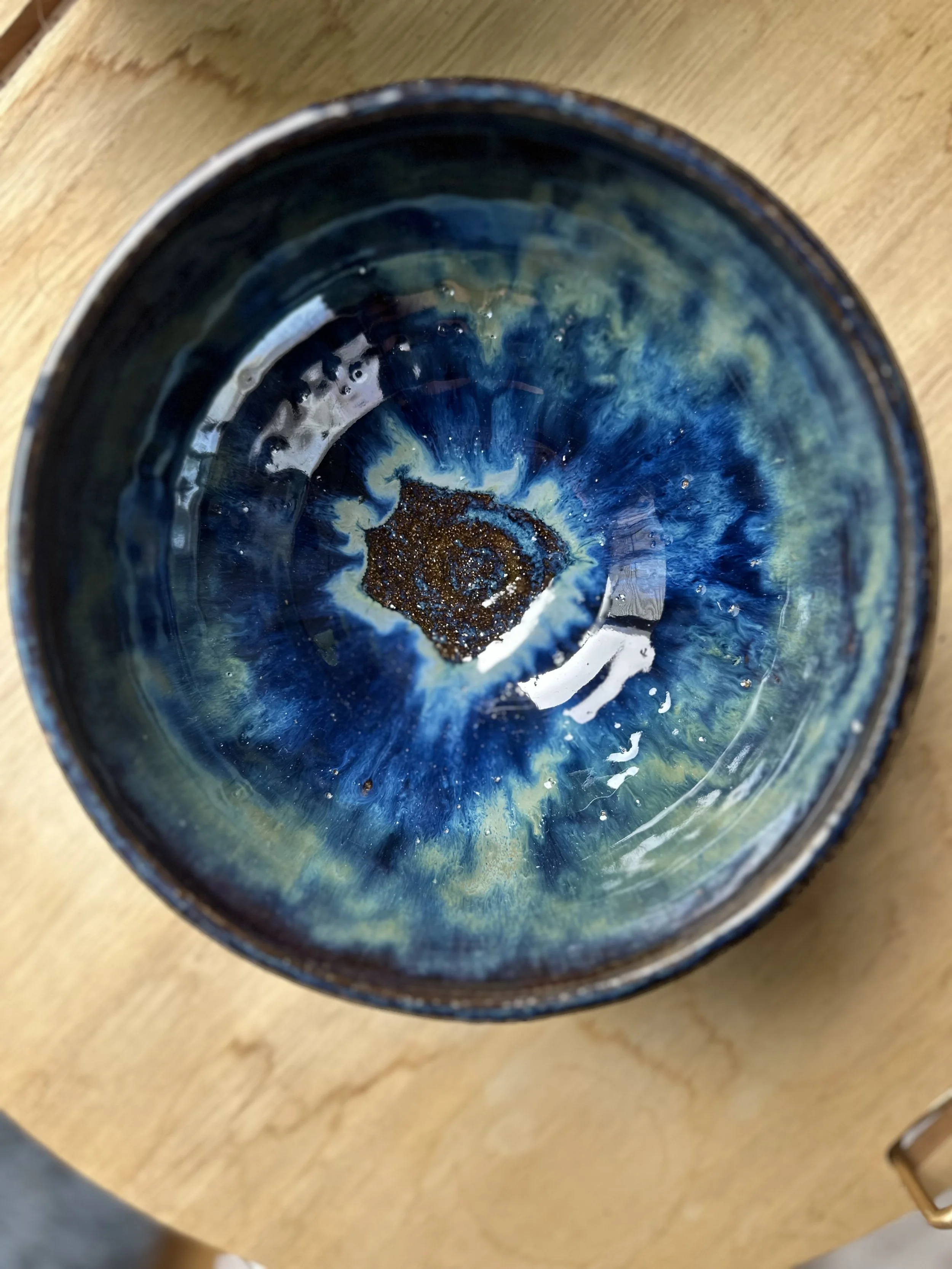 Close-up of a dark blue and green glazed ceramic bowl with a textured and glossy interior, placed on a wooden surface.