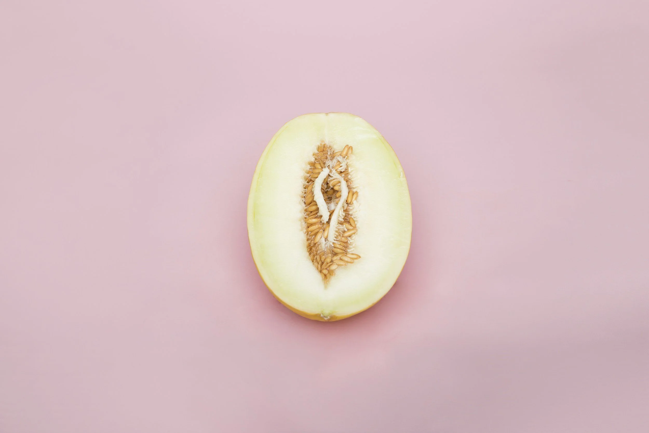 Halbierte Melone mit sichtbarem Fruchtfleisch und Samen auf einem pinkfarbenen Hintergrund.