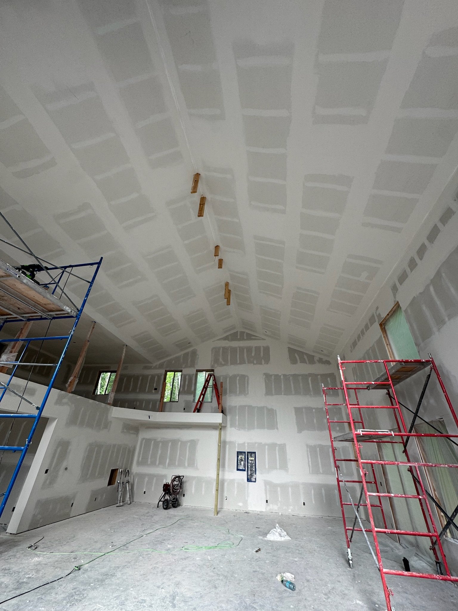 Interior of a building under construction with drywall walls and ceiling, scaffolding on the left and right sides, and construction tools on the floor.