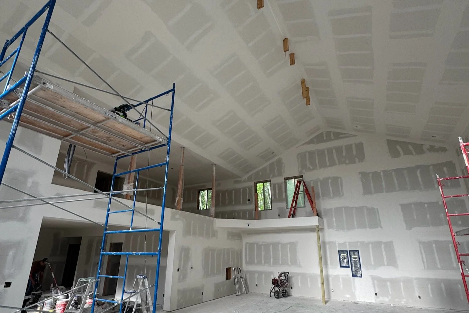 Interior of a house under construction with unfinished drywall, scaffolding, ladders, and construction tools.