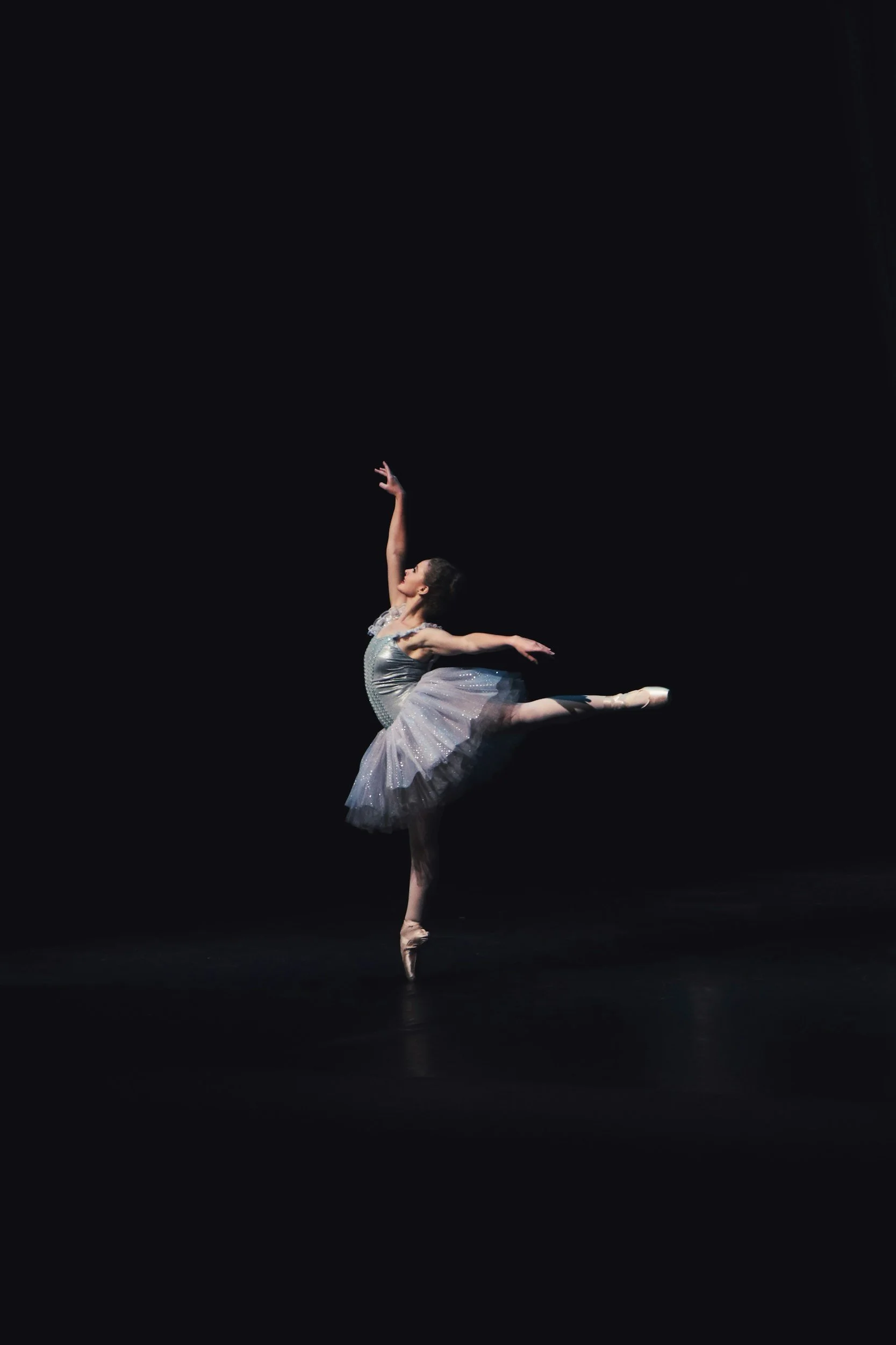 A ballerina performing an arabesque on stage with a dark background, wearing a sparkling ballet costume.