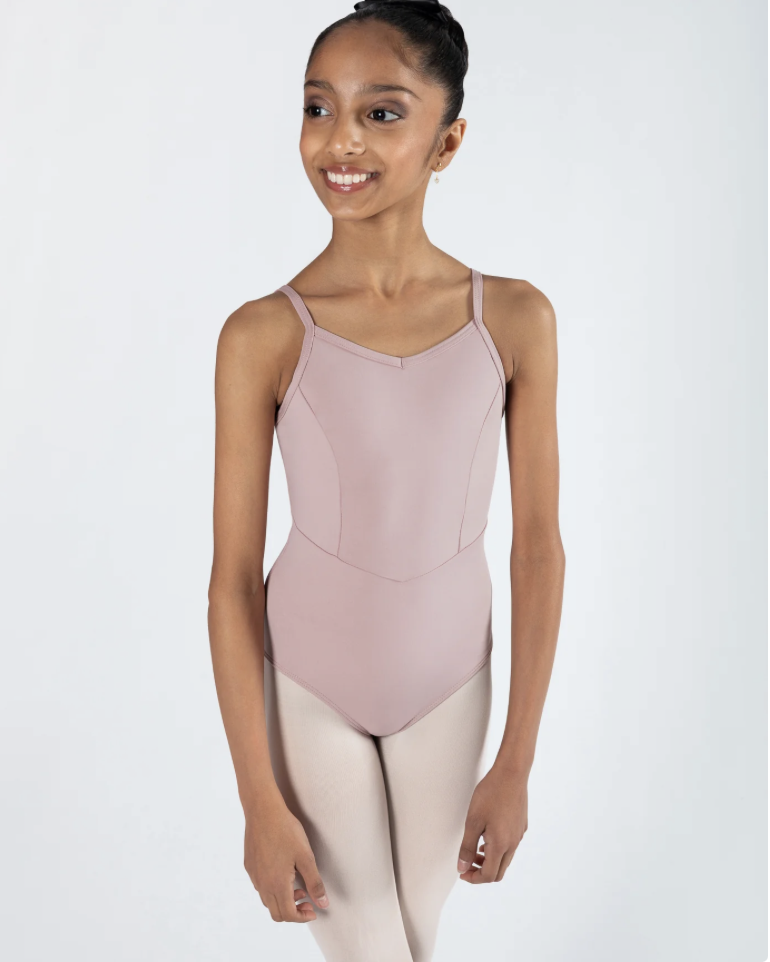 Young ballerina girl in pink leotard and beige dance tights smiling and looking to the side against a plain white background.