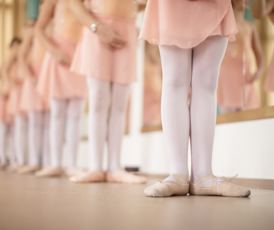 Ballet dancers in pink tutus and white tights standing in a line, focusing on their legs and feet, preparing for a performance.