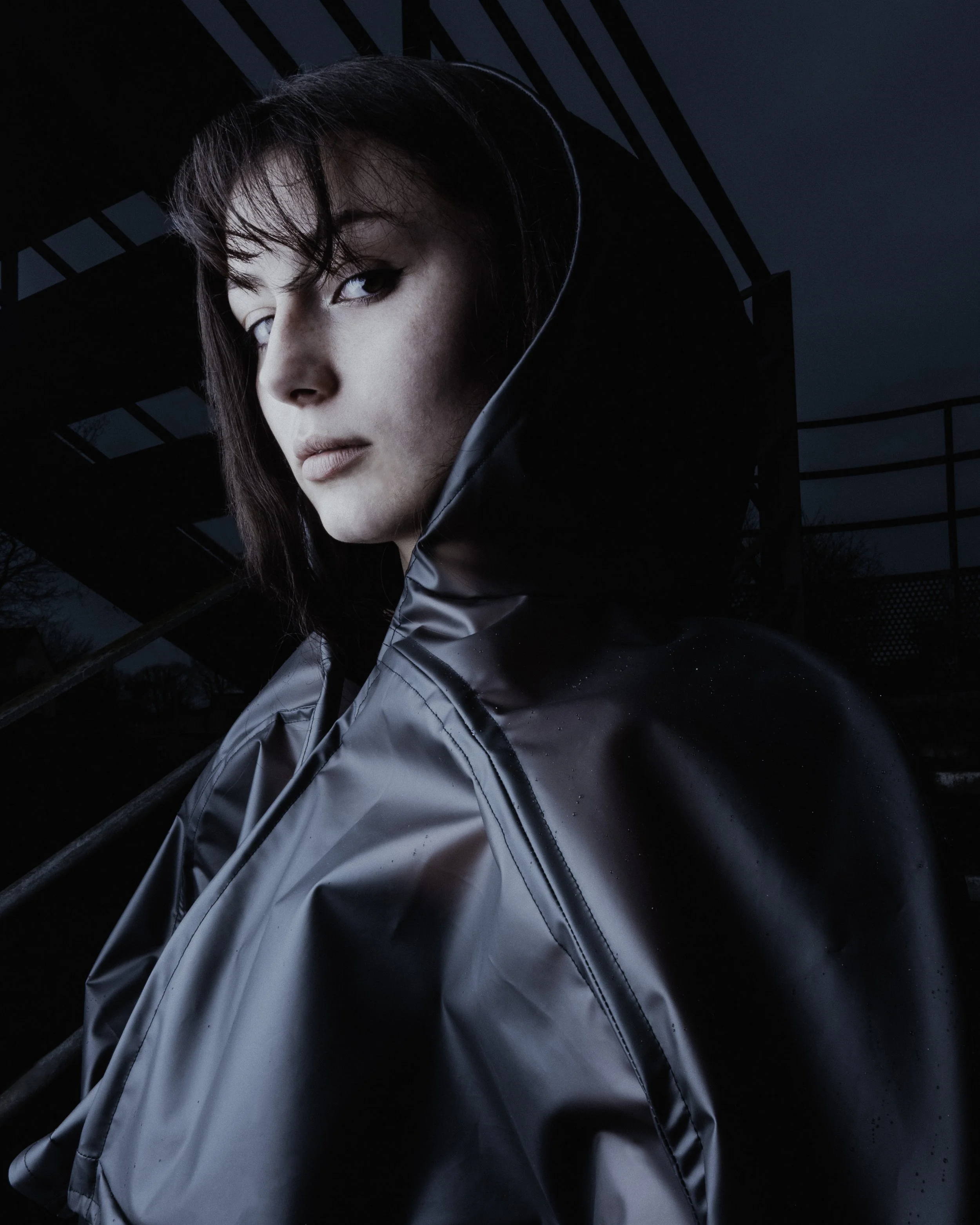 Portrait d'une femme portant une veste en tissu foncé, avec un paysage urbain nocturne en arrière-plan.
