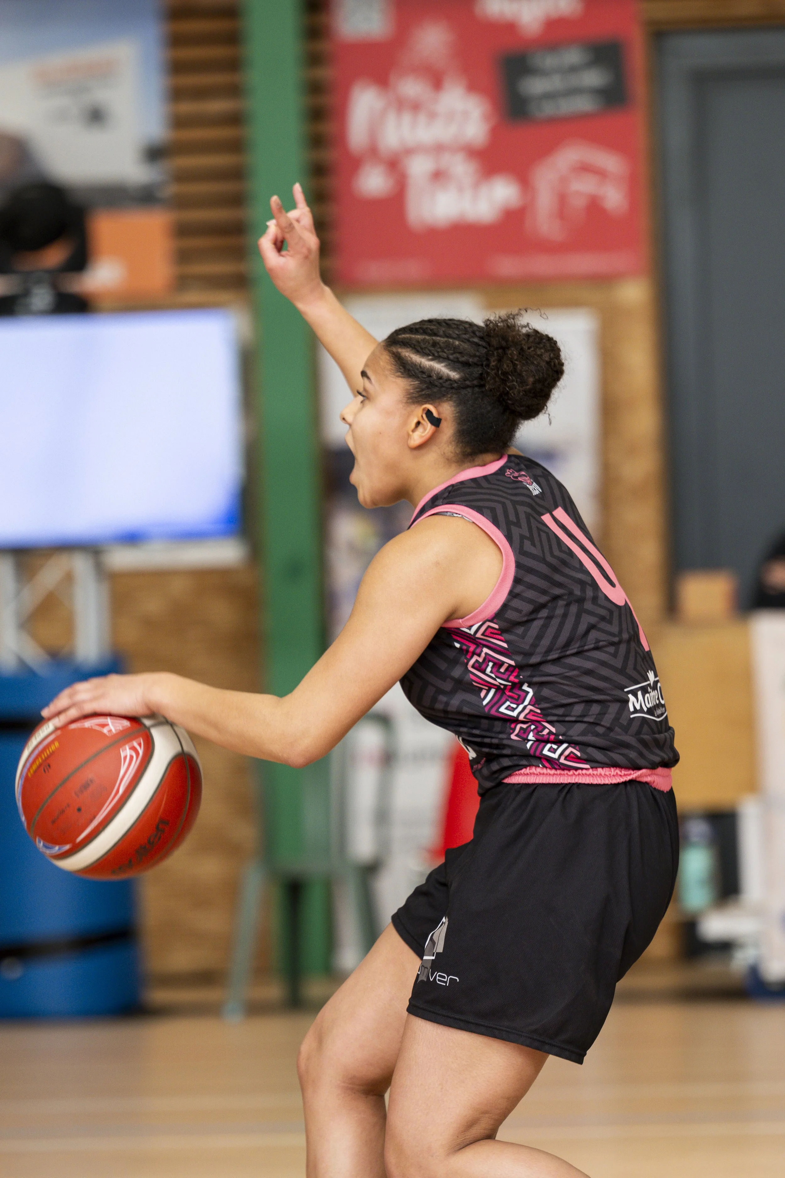 Une joueuse de basketball en train de dribbler avec le ballon dans une salle de sport, portant un maillot noir et des shorts noirs.