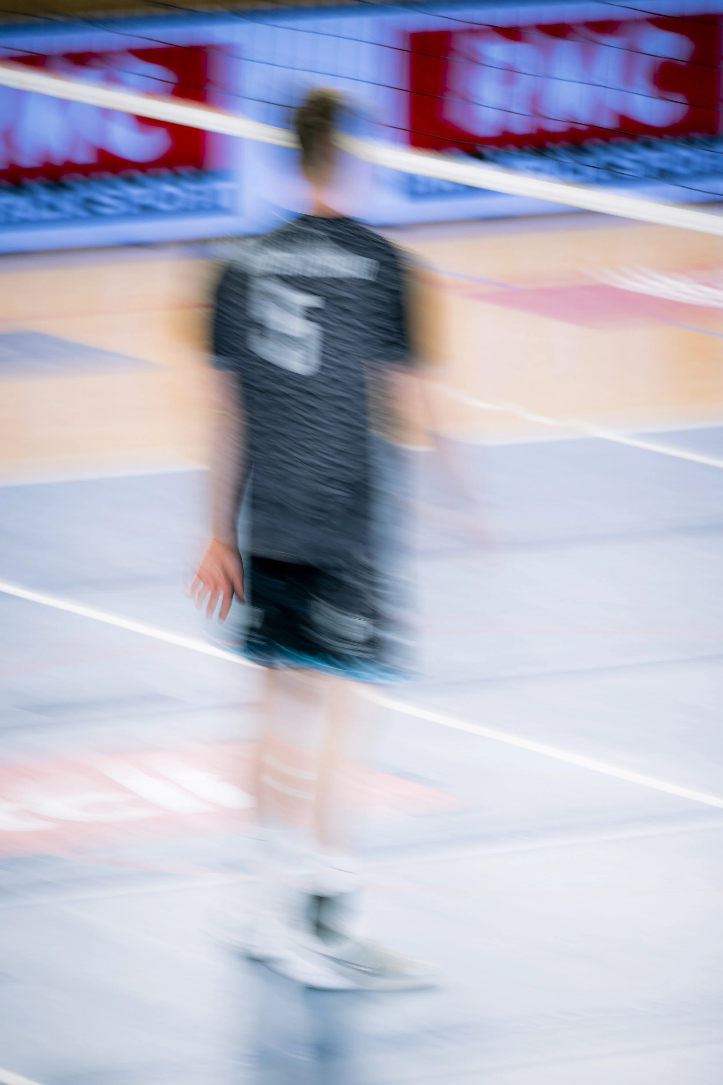Un joueur de volleyball sur un terrain d'intérieur en mouvement, flou artistique, portant un maillot noir avec un chiffre.
