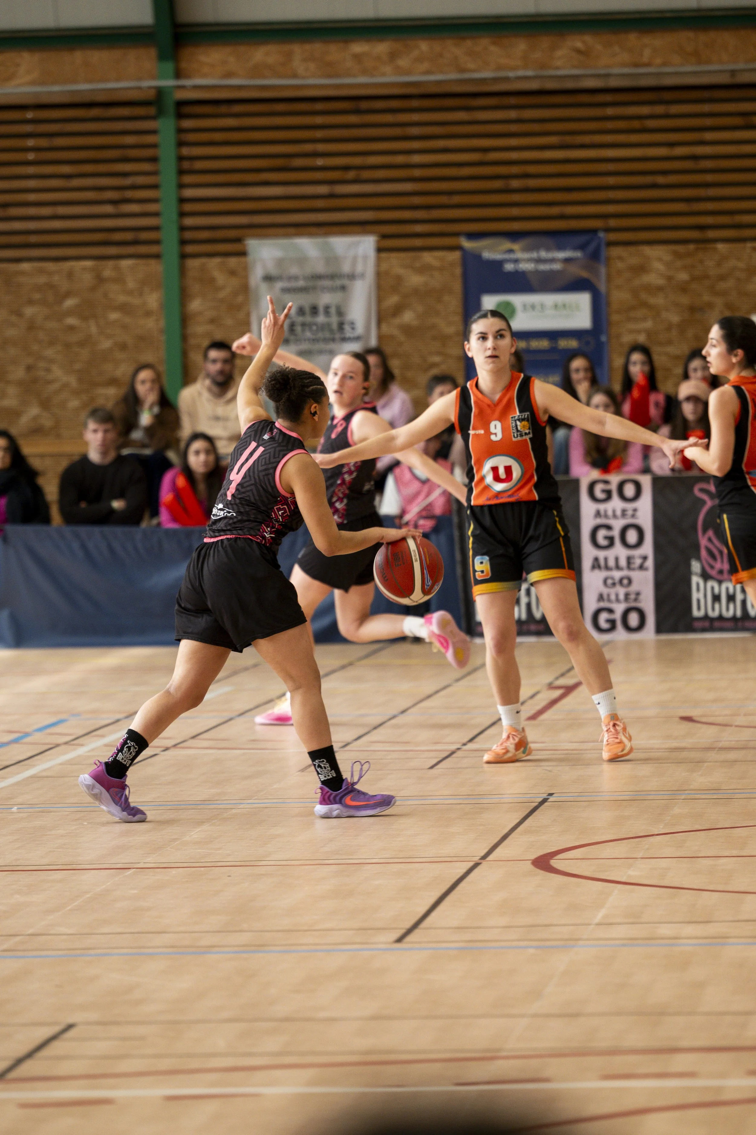 Joueuses de basketball en action lors d'un match intérieur, avec un public en arrière-plan.