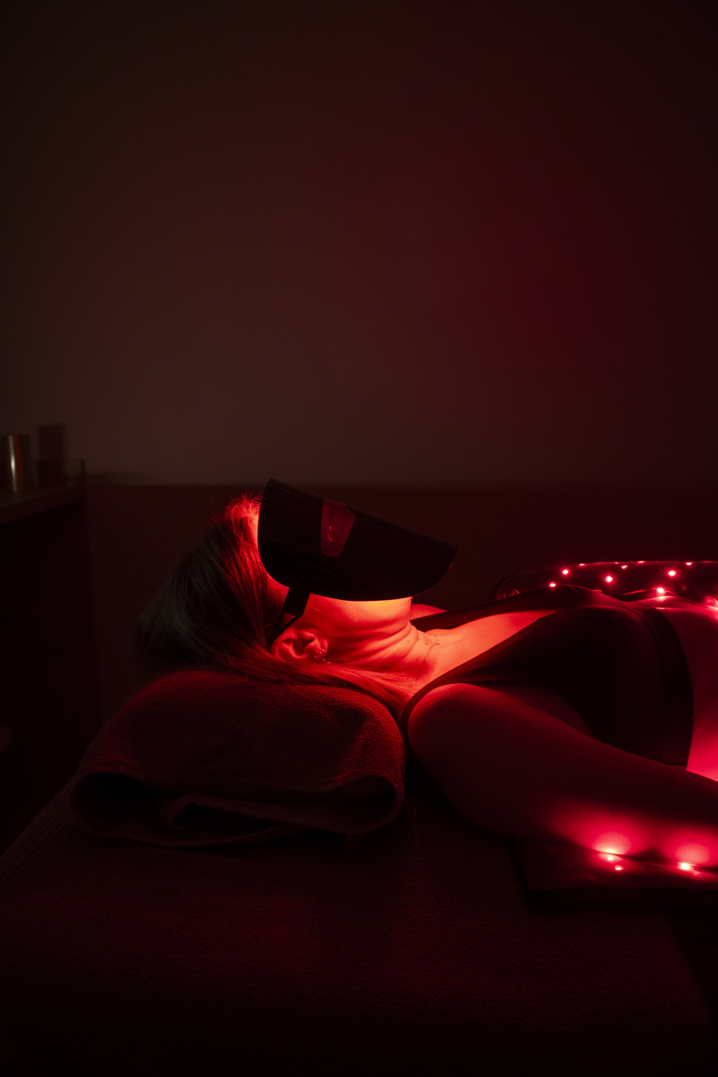 Une femme allongée sur un lit, recevant un traitement de luminothérapie avec une lampe émettant une lumière rouge.