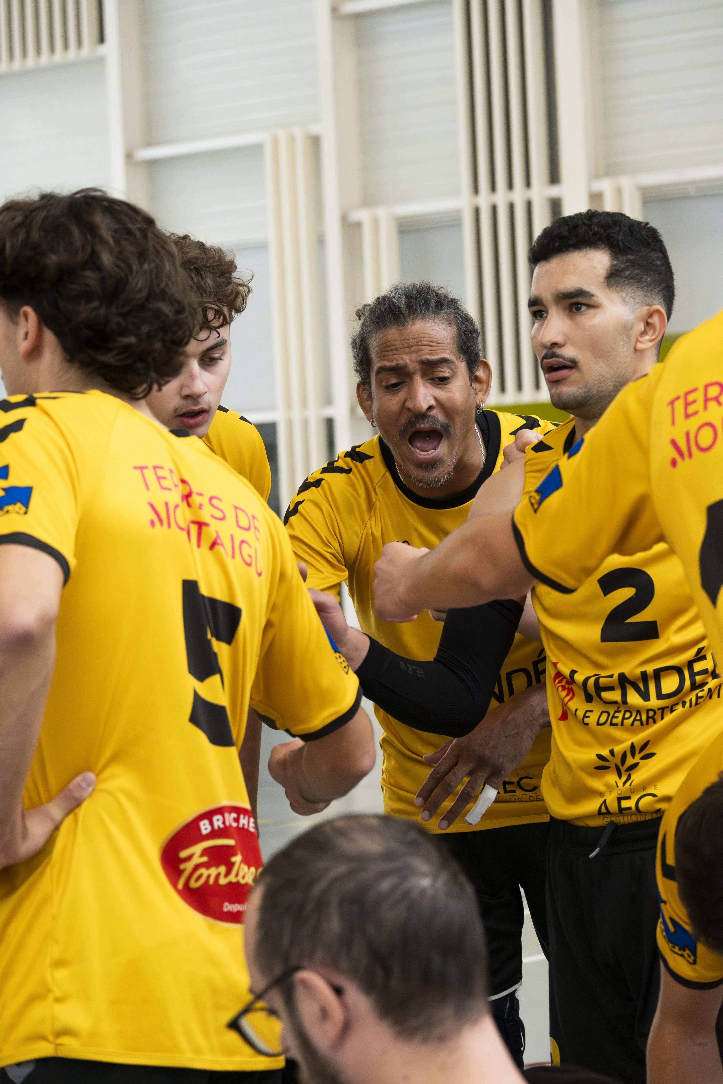 Une équipe de joueurs de volleyball en jaune en pleine discussion dans une salle