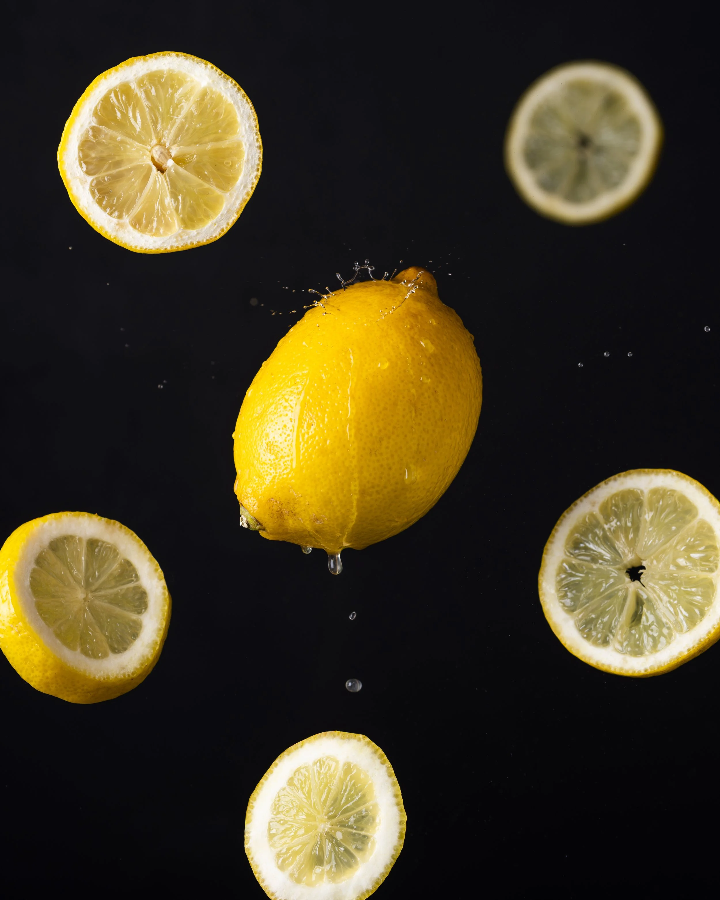 Tranches de citron et citron entier dans un liquide, avec un fond noir.