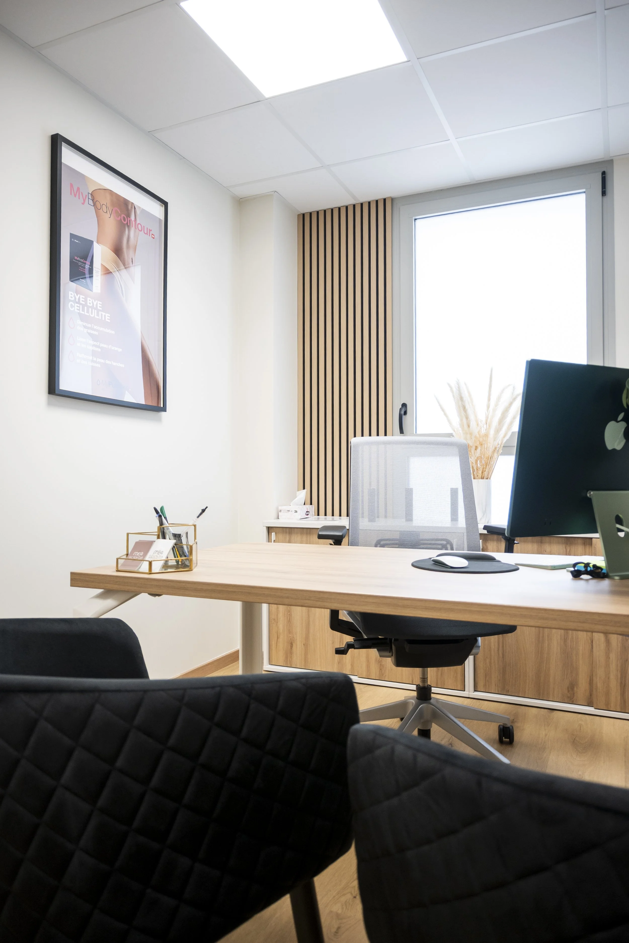 Une salle de bureau moderne avec un bureau en bois, une chaise de bureau, un ordinateur portable, un écran d'ordinateur, une plante décorative, une fenêtre avec volet en bois, une affiche publicitaire sur le mur, un bureau avec des fournitures, et un décor épuré.
