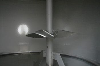 Close-up of a metallic rotor blade attached to a vertical pole inside a metallic tank or container.