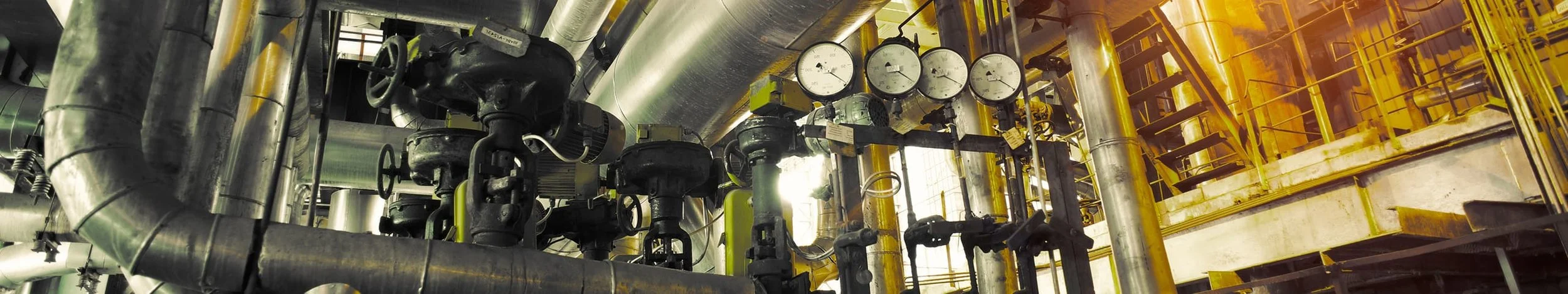 Industrial piping system with gauges, valves, and metal pipes in a factory or processing plant.