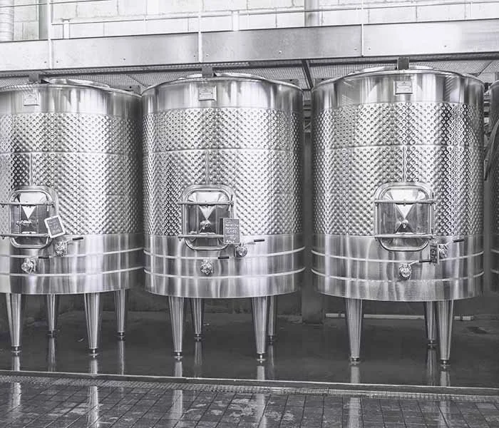 Three large stainless steel fermentation tanks in a brewery or winery.