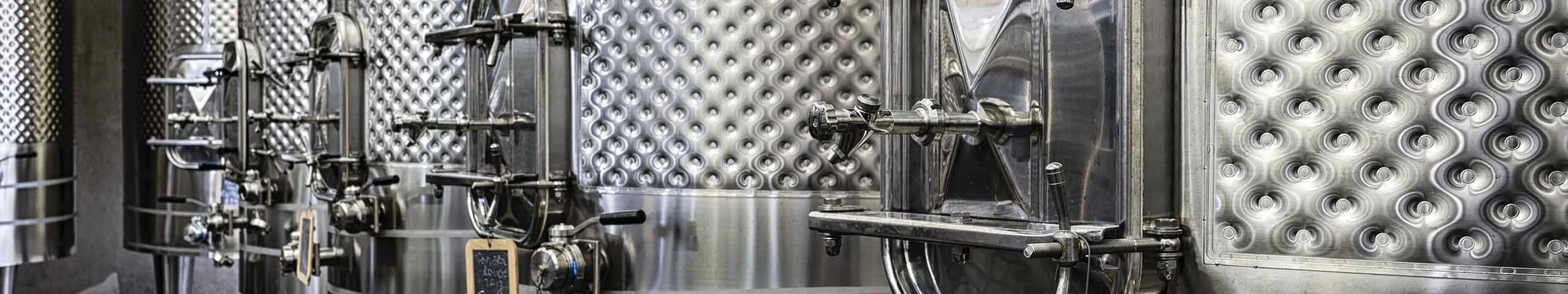 Close-up of stainless steel wine or beverage tank with various valves and gauges.