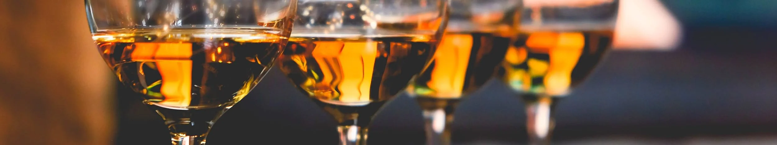 Close-up of four glasses of amber-colored whiskey on a dark background, with reflections and a blurred setting.