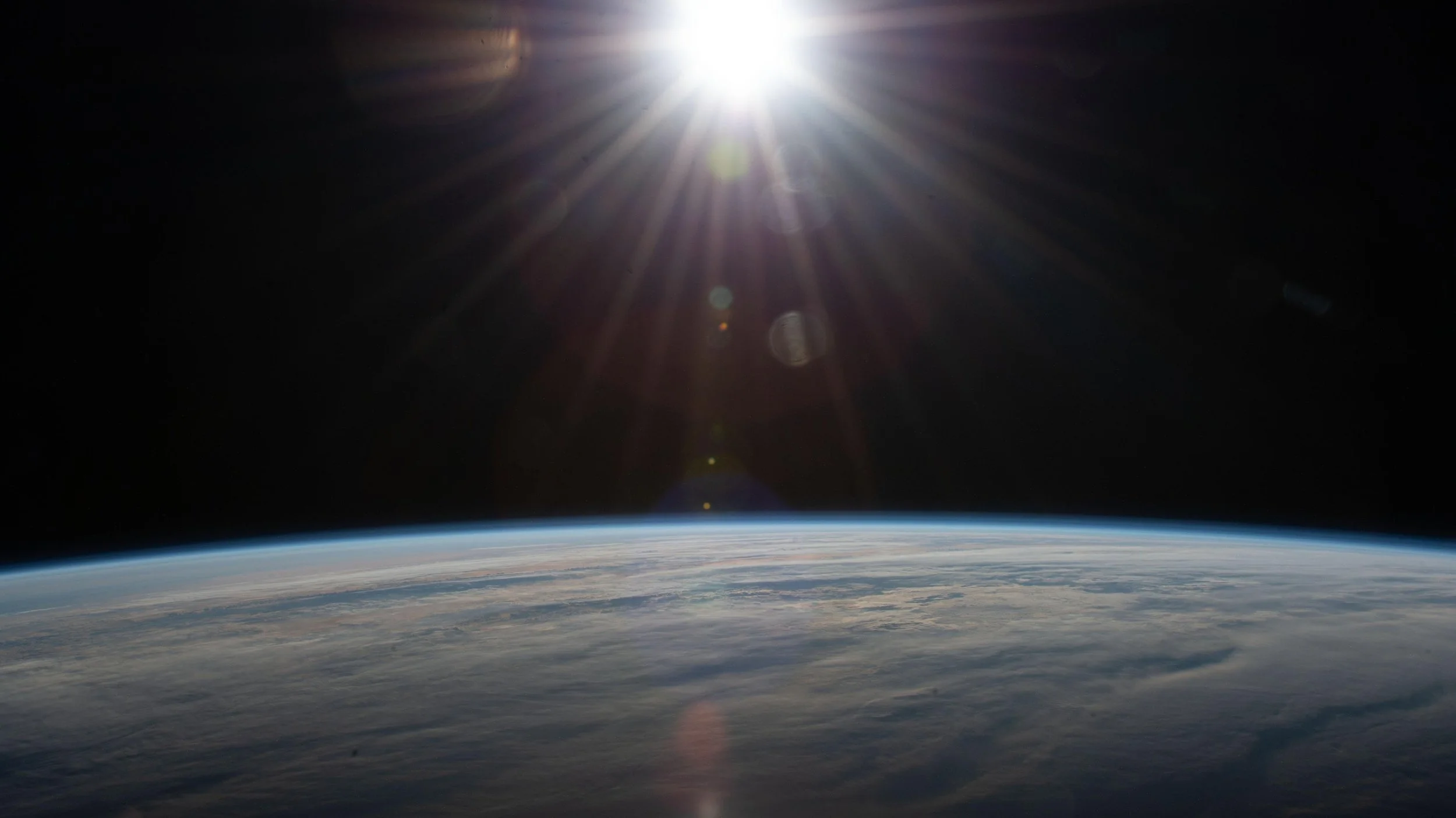 Photo of Earth viewed from space with the Sun shining overhead, creating lens flares and light rays in space