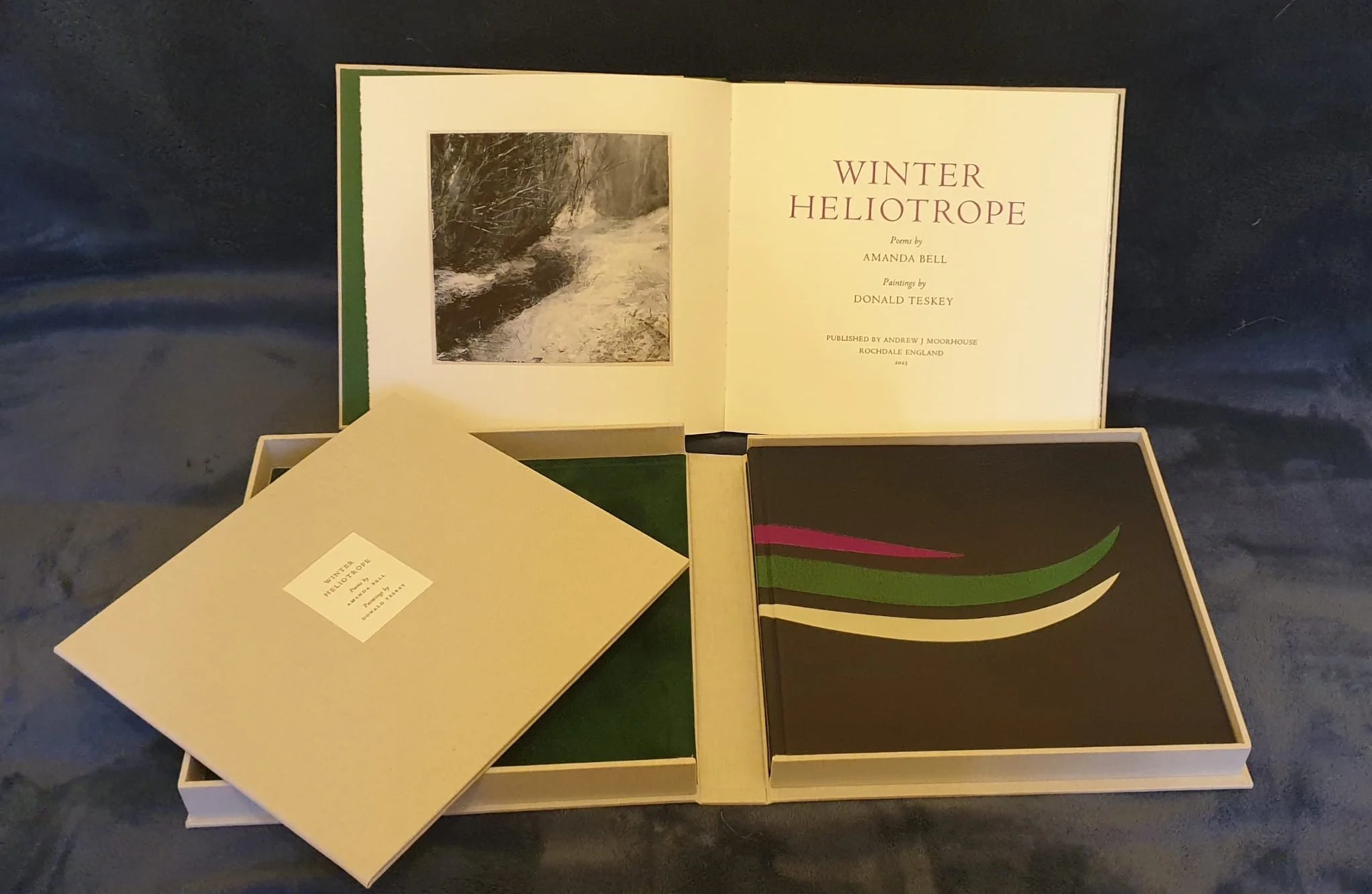 Open book titled "Winter Heliotrope" with poems by Irish author Amanda Bell and paintings by Donald Teskey, published in Rochdale, England, 1981; dark background, book on display, several other items partially visible.