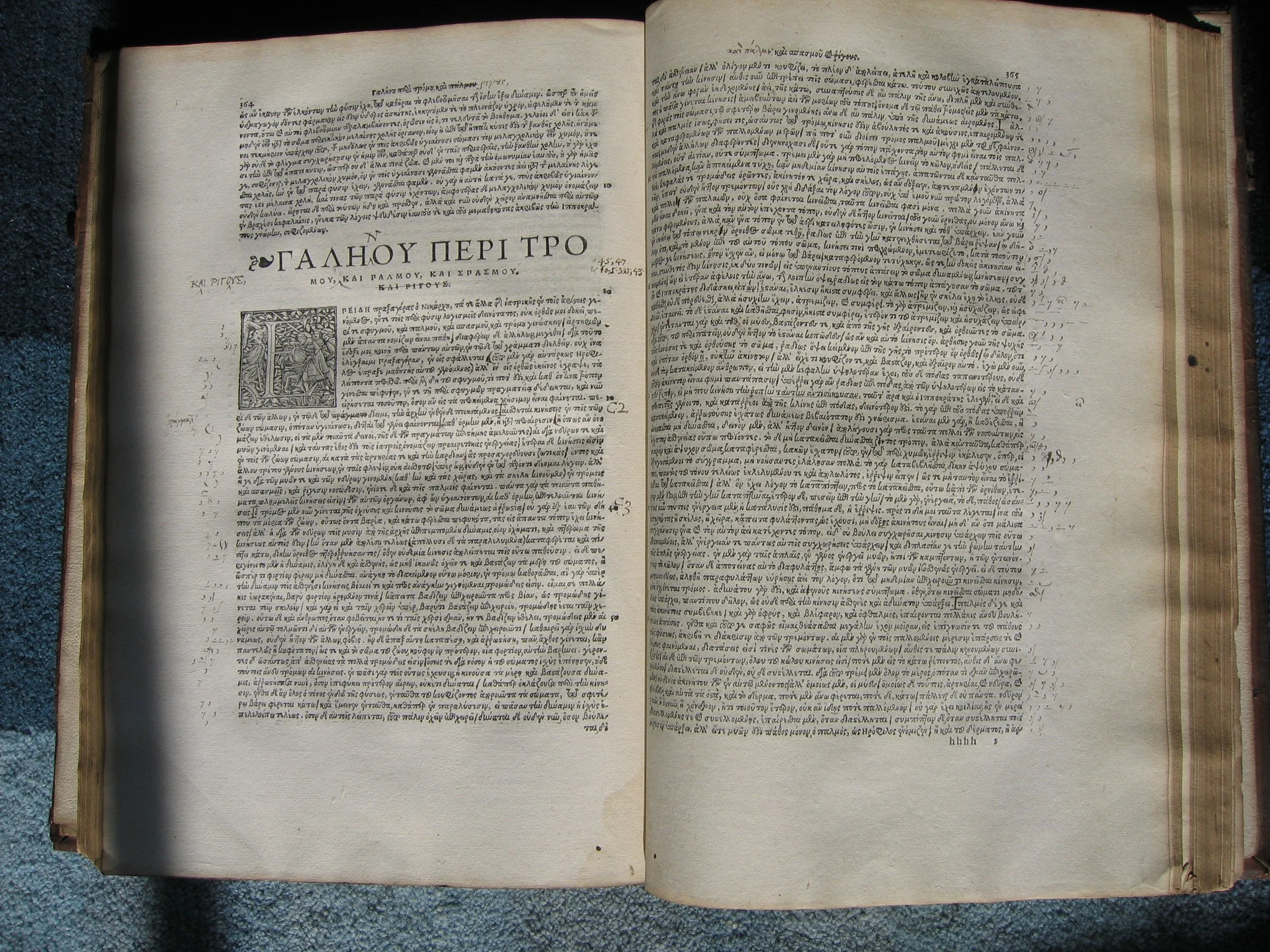 An open old book with handwritten text in Greek, showing a decorative initial letter and a small illustration on the left page.