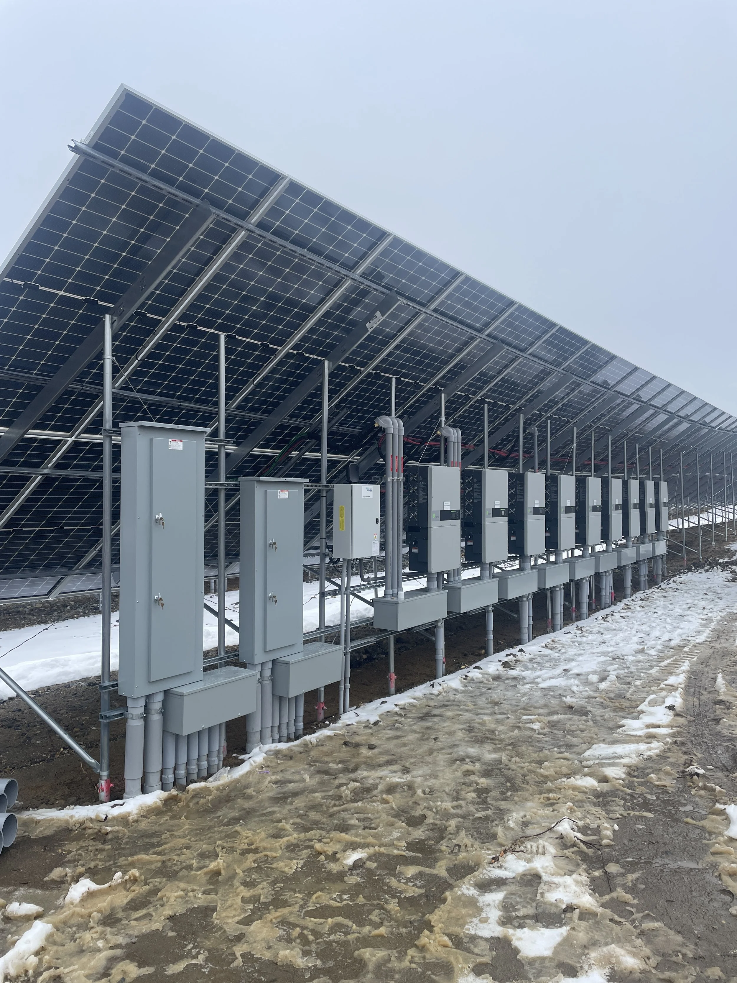 A row of solar panels installed outdoors on a cloudy winter day with snow and ice on the ground.