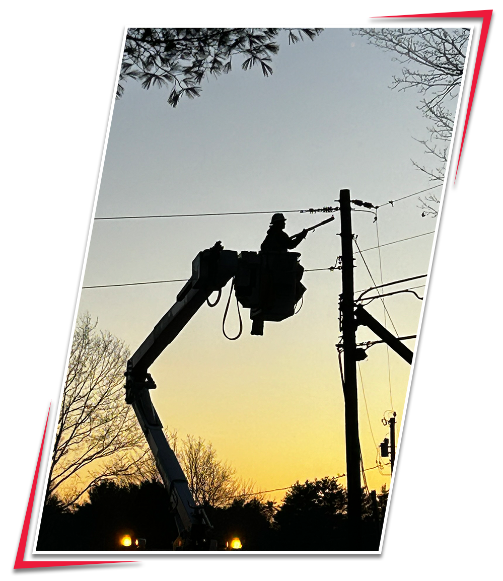 Electrician working on power lines while elevated in a bucket lift during sunset.