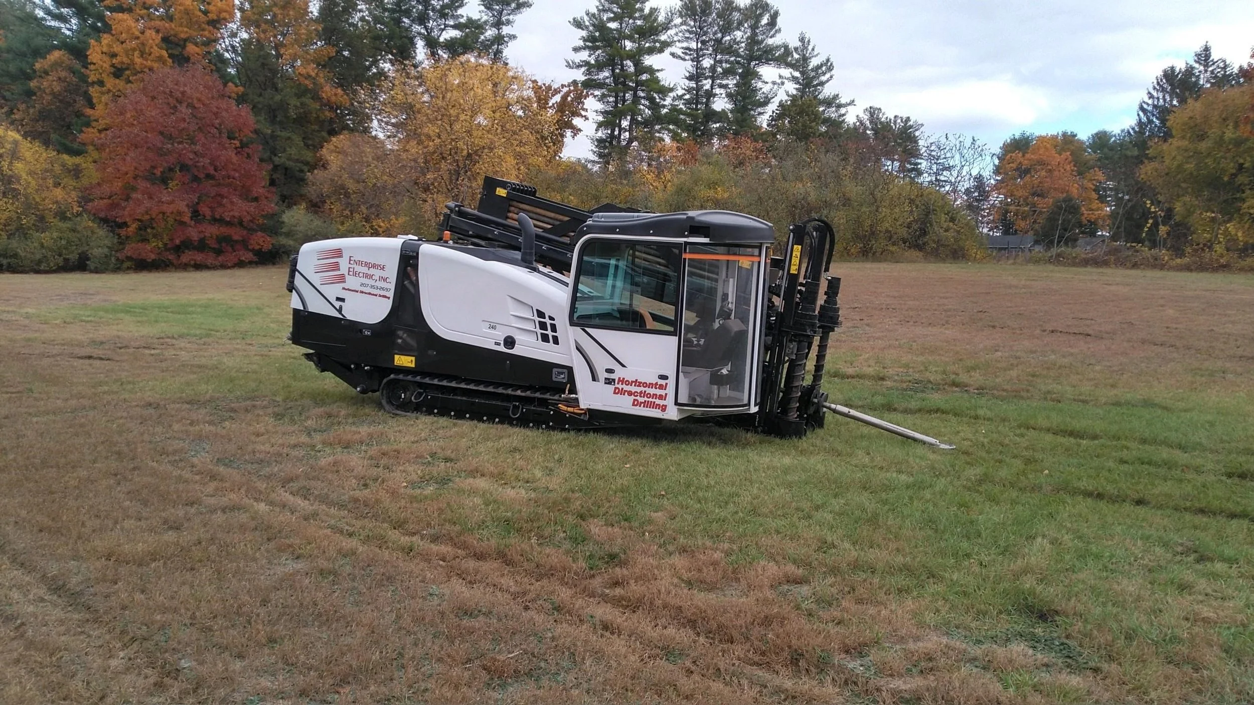 A horizontal directional drilling machine outdoors on a grassy field with trees and colorful autumn foliage in the background.