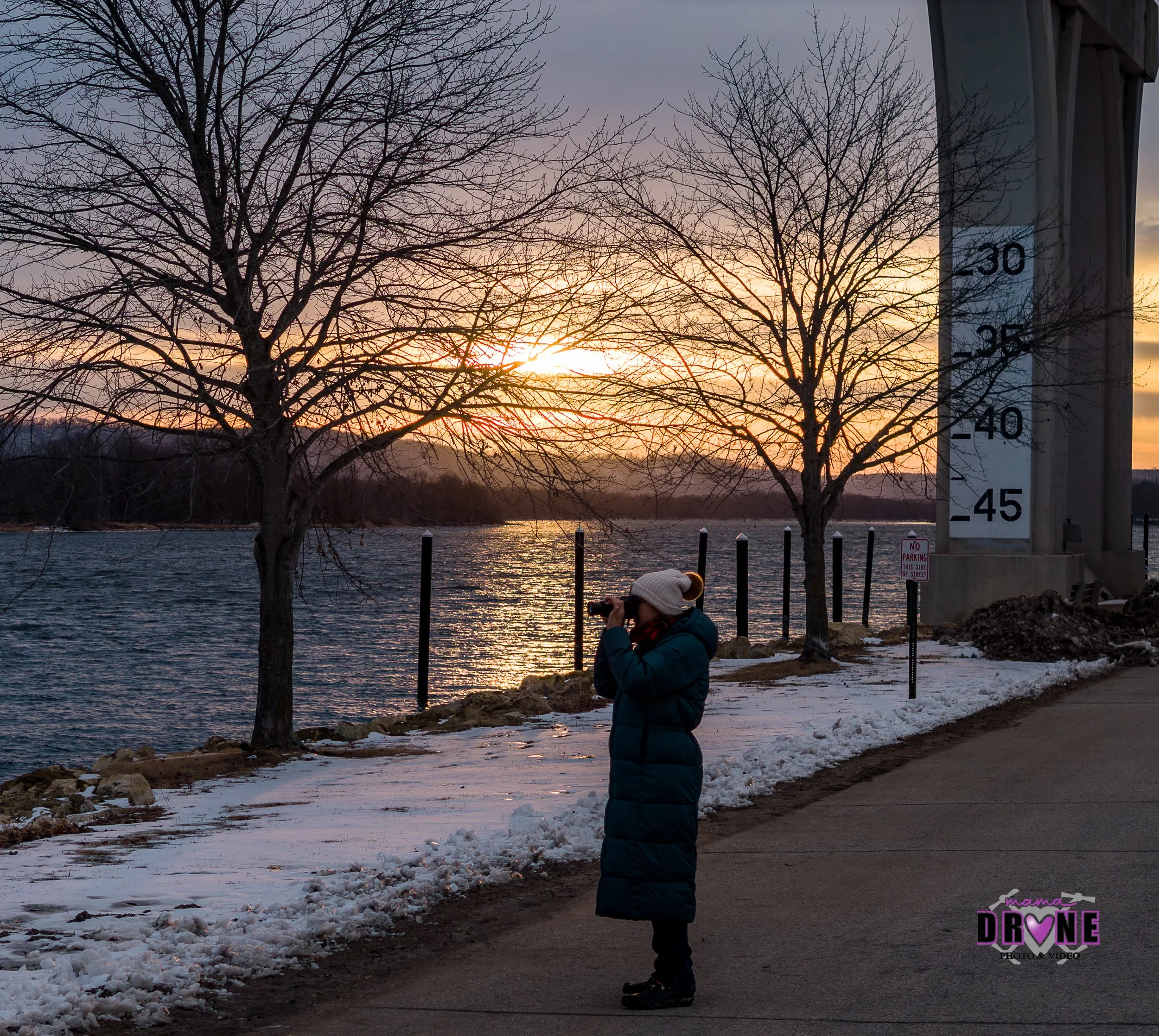 Sunset winter river scene with snow and open water. Includes a person with a long winter parka and white hat looking at the water.