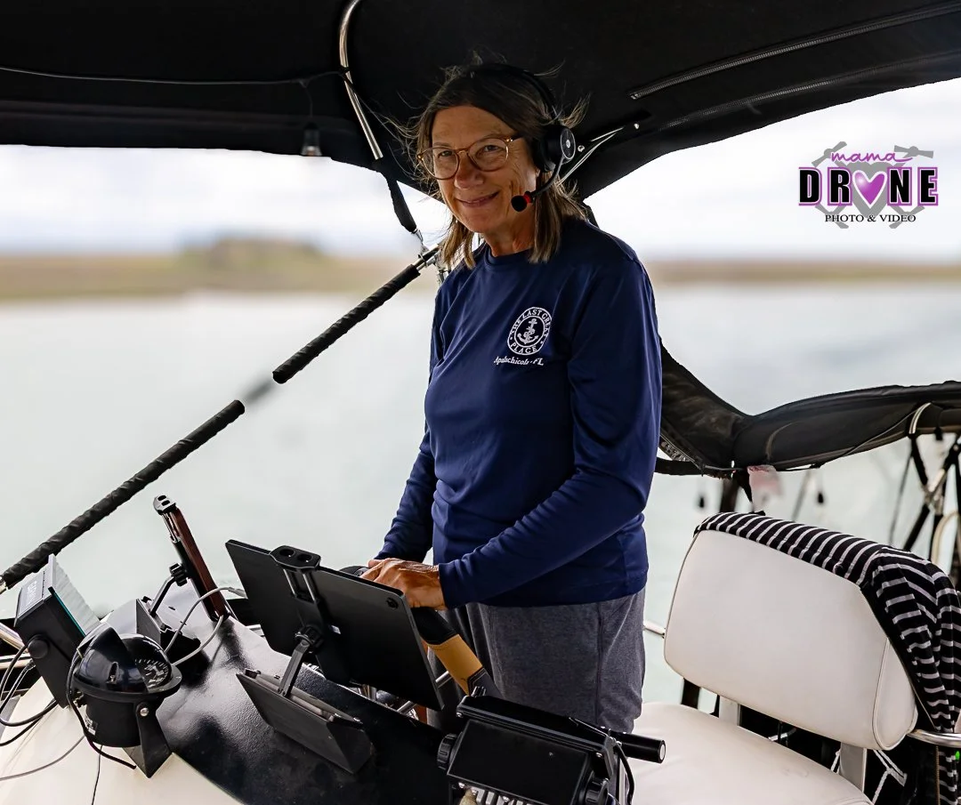 Woman with long sleeve blue shirt and grey pants, glasses and headphones driving a large boat.
