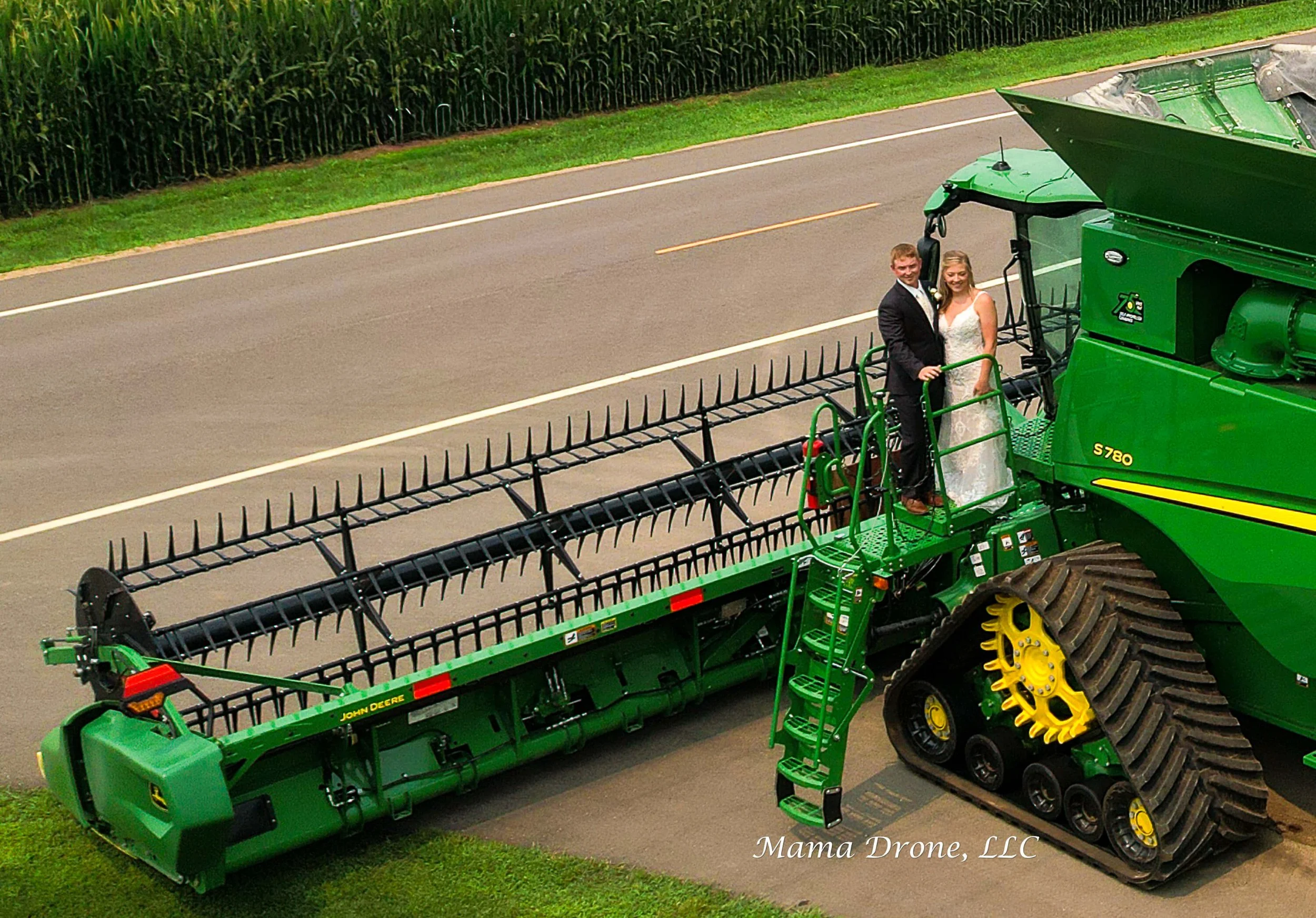 Man in black suit with woman in white dress on a green and yellow tractor near a highway.