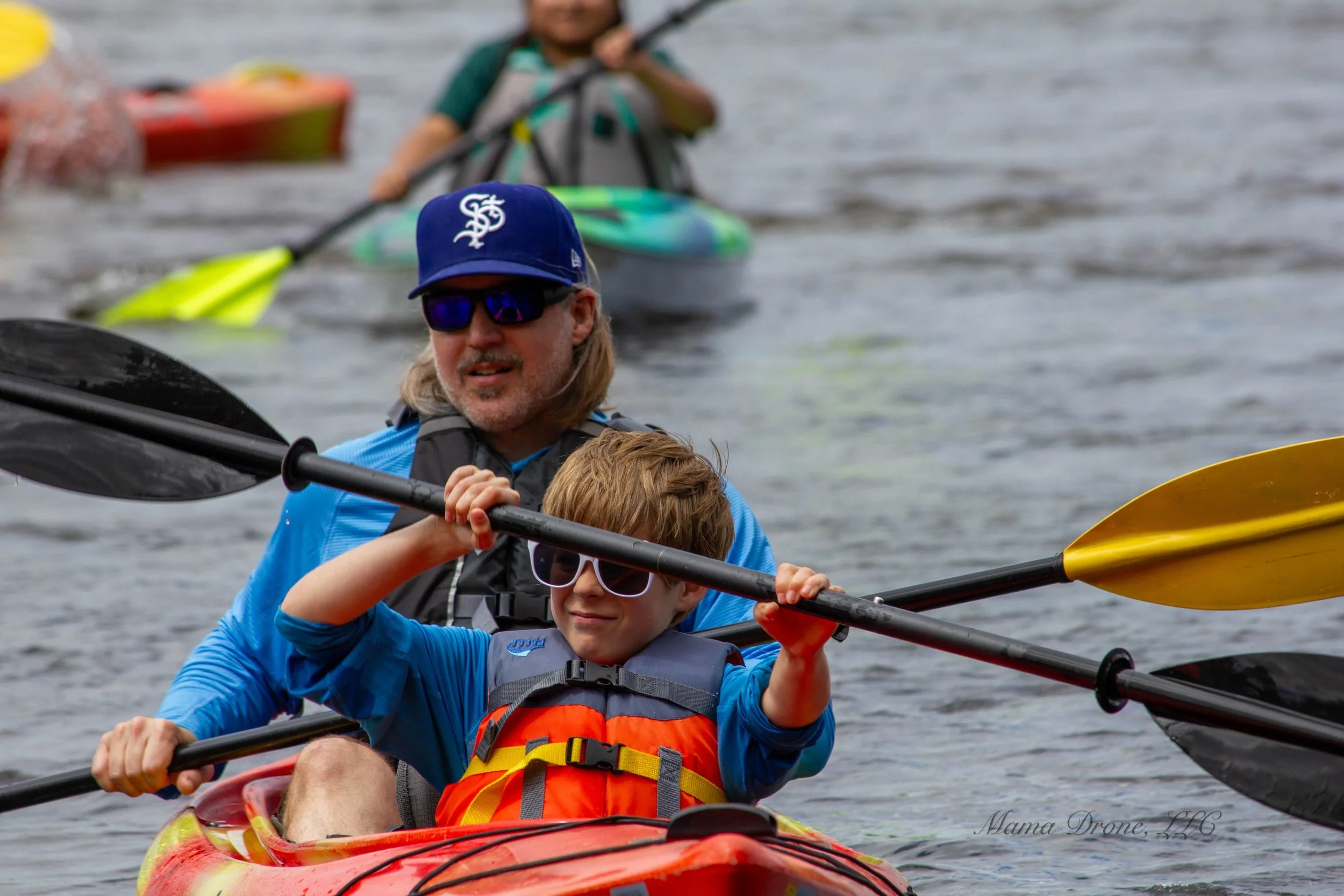 Father and young son kayaking together with others in background.

