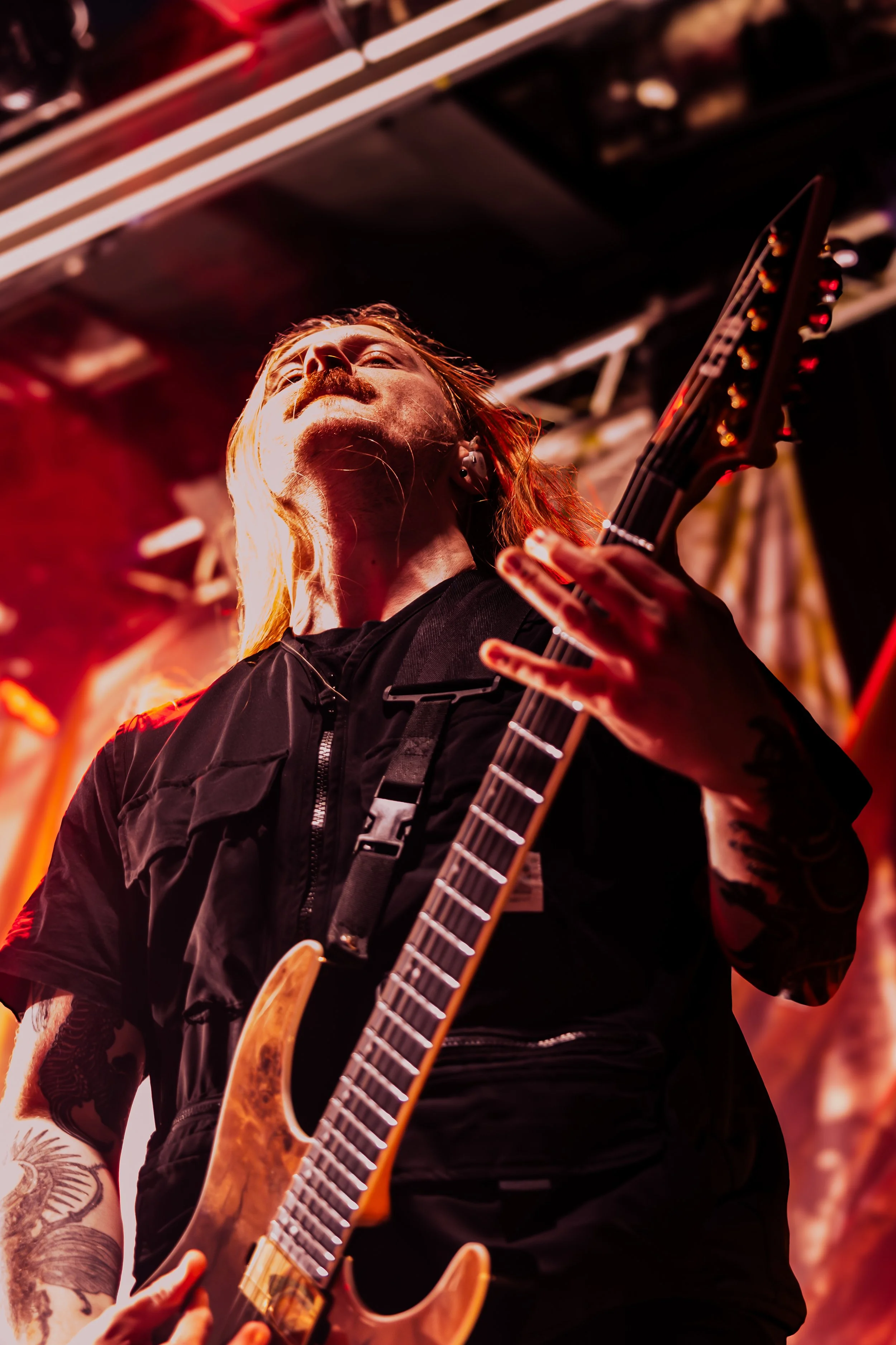 A person playing an electric guitar on stage, with long hair and tattoos.
