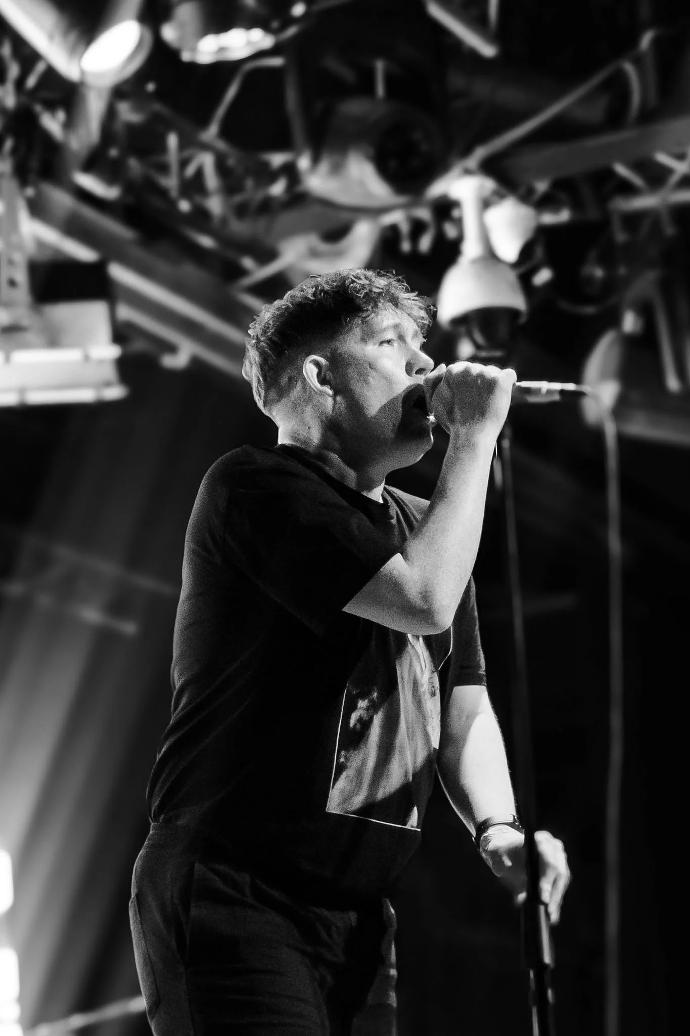 A young man singing into a microphone on stage with blurred background.