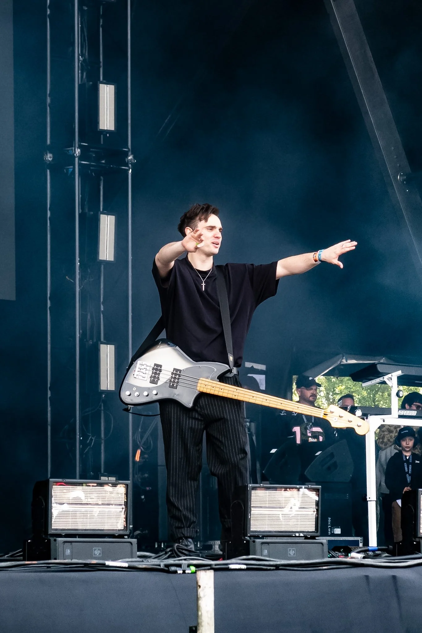 A person playing an electric bass guitar on a stage during a live performance, with speakers and audio equipment visible around him.