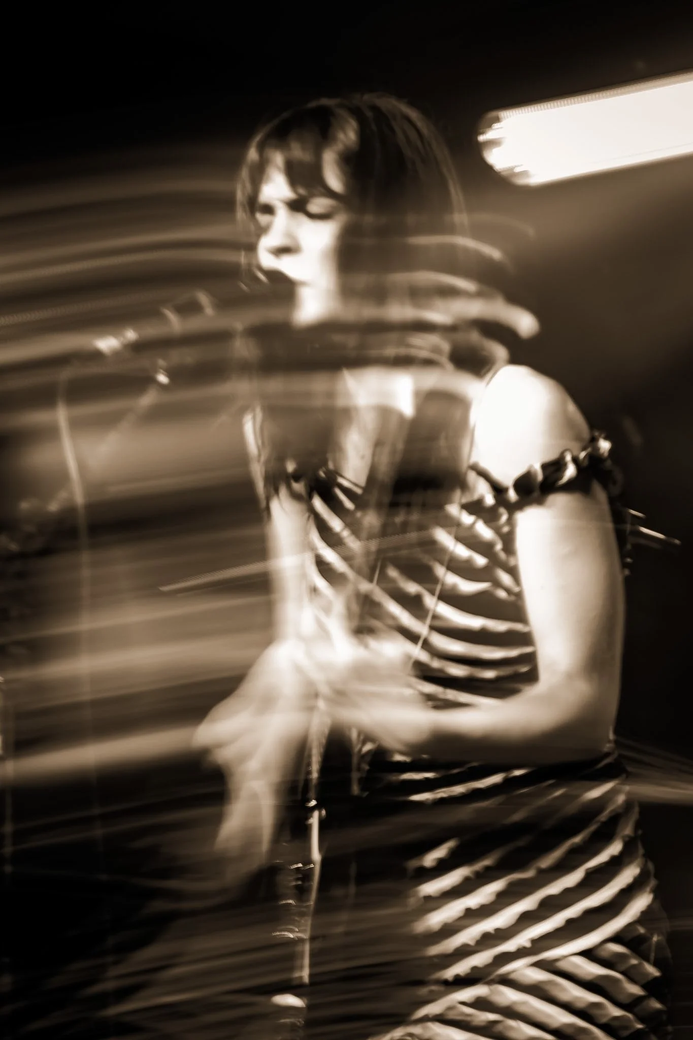 Black and white photo of a woman with short dark hair, wearing headphones, possibly in a recording studio, with motion blur streaks across the image.