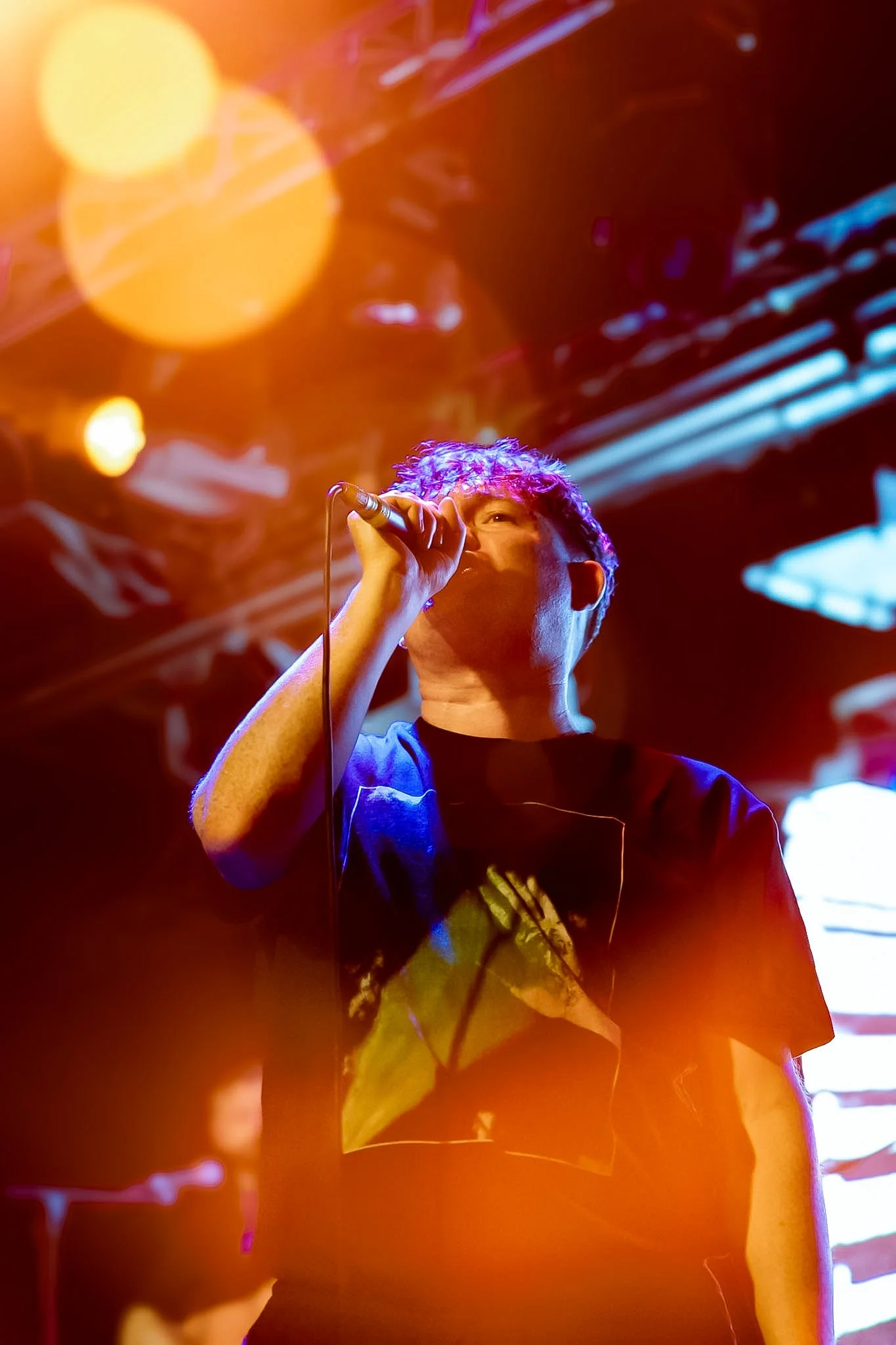 A person singing into a microphone on stage with colorful lighting and abstract background.