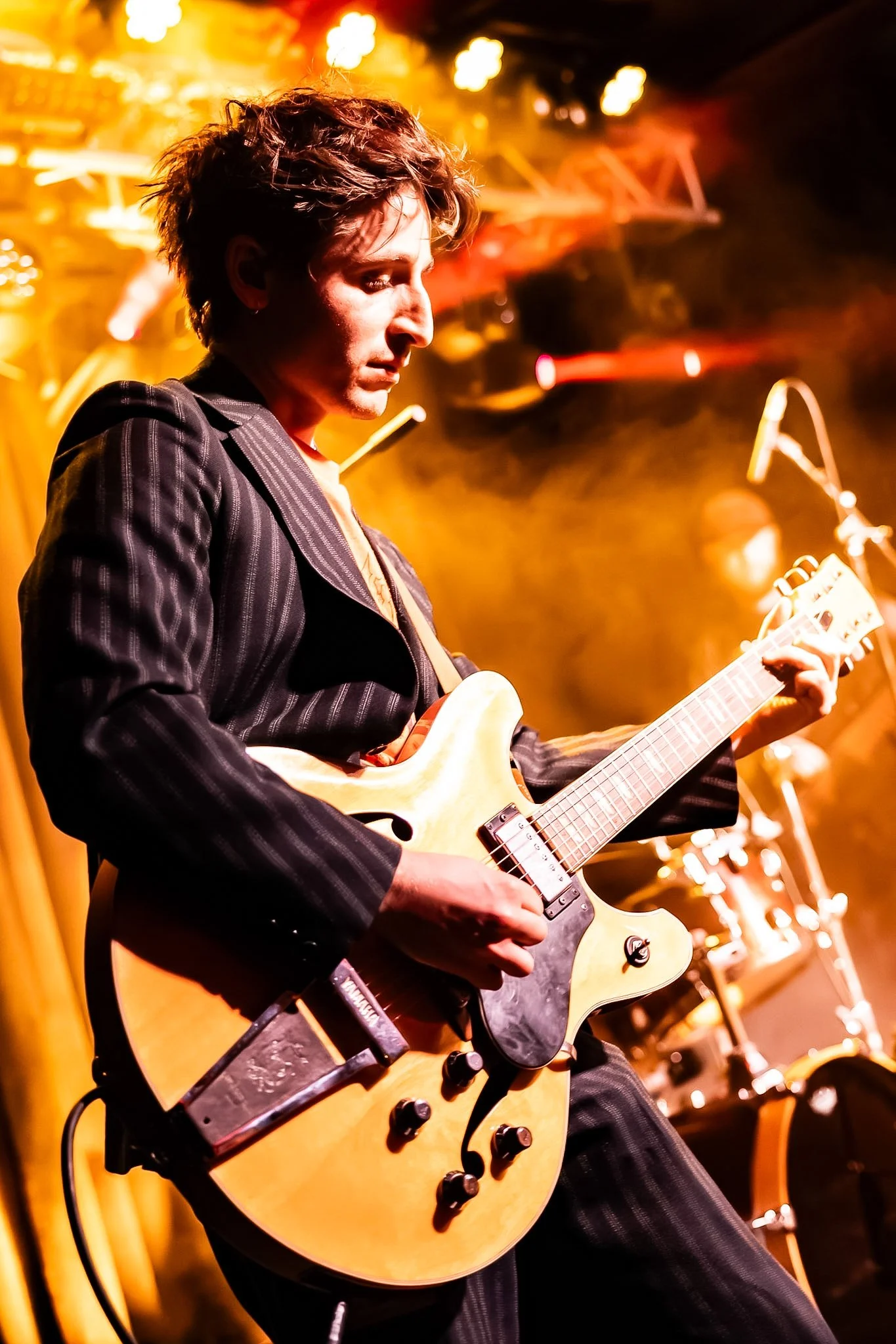 A man playing an electric guitar on stage with yellow and red lighting.