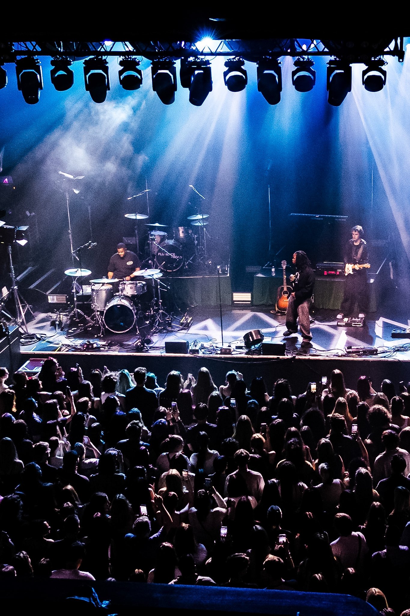 Stage with bright lights, drum set, guitar, and keyboard, audience watching a concert.