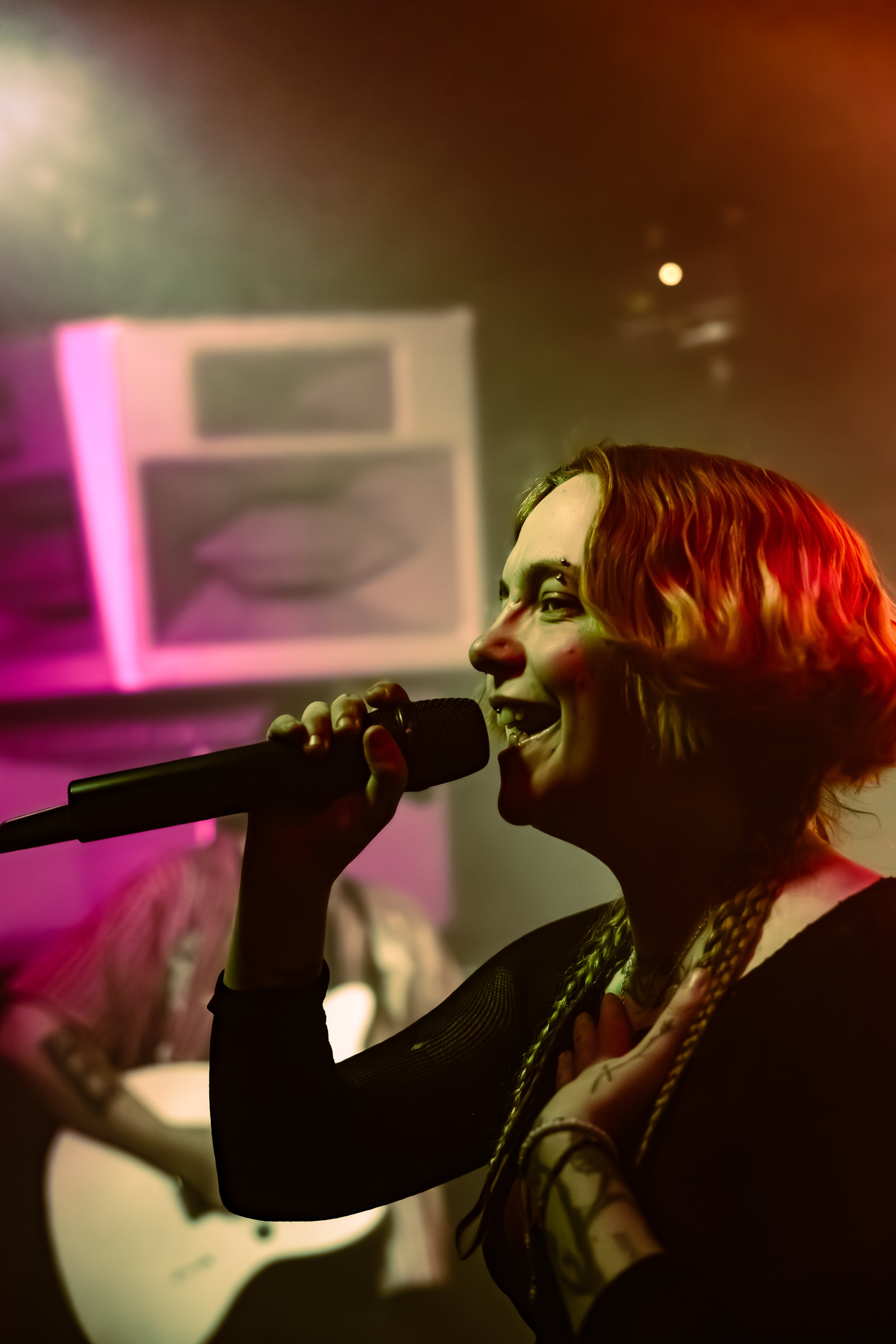 A person with a painted face singing into a microphone with a colorful abstract background.