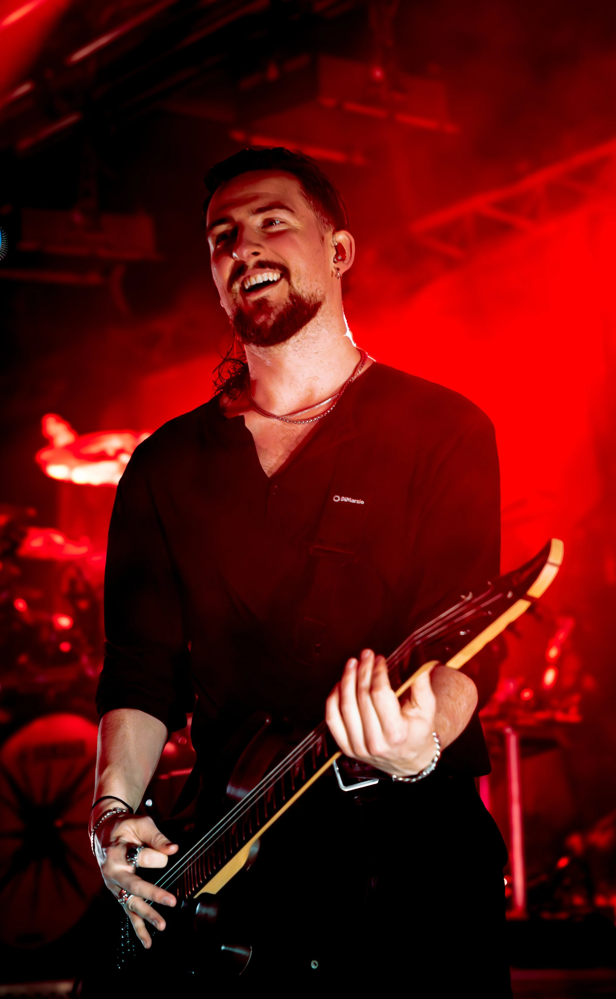 A man playing an electric guitar on stage surrounded by red lighting.