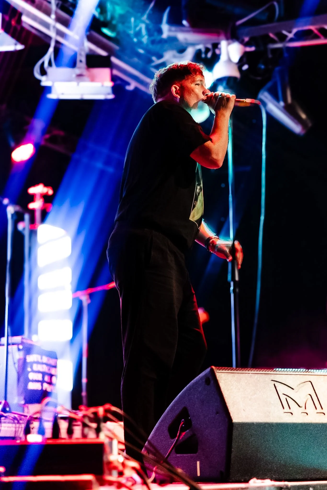 A person singing into a microphone on stage with colorful stage lighting.