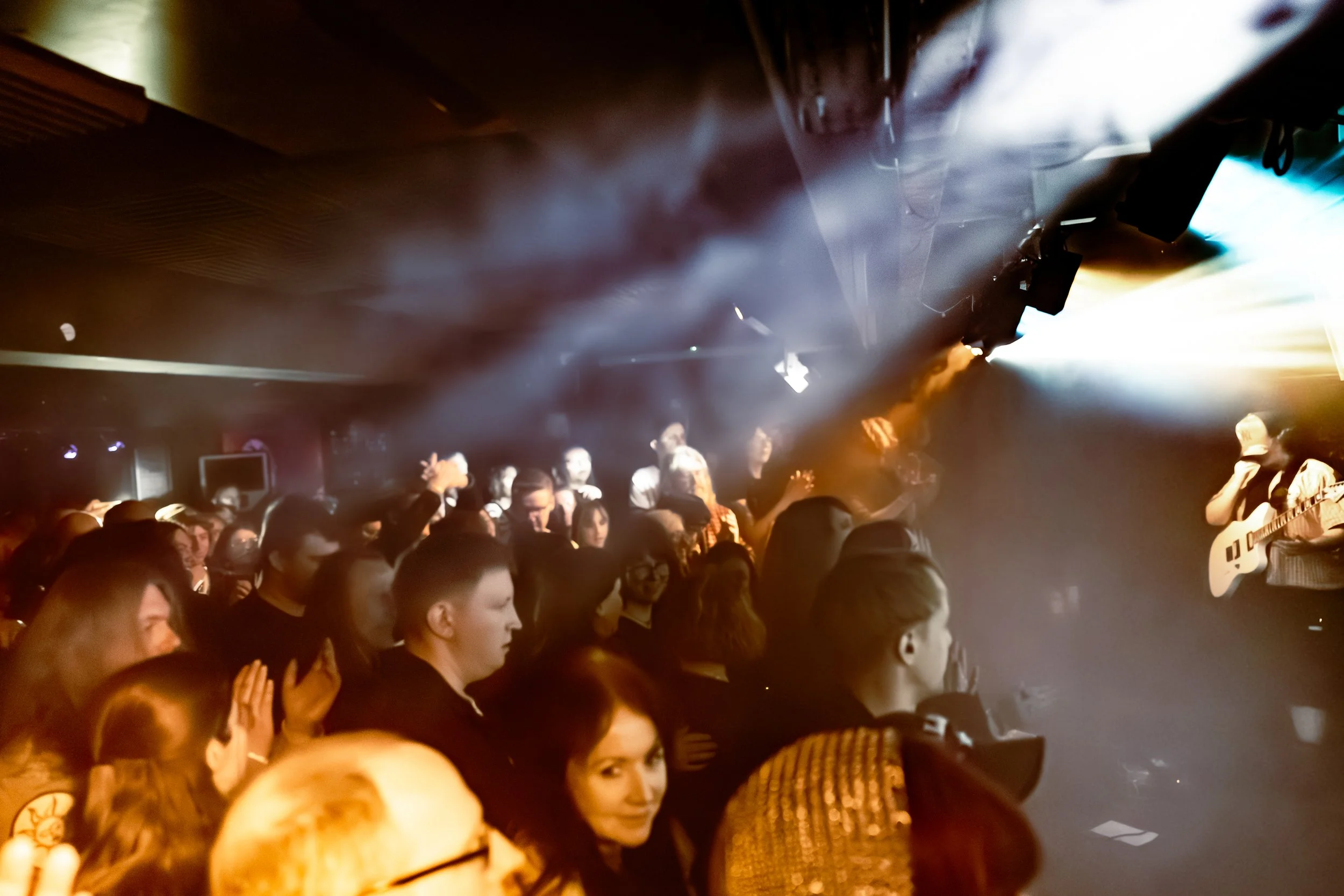Crowd of people at a concert or event, with stage lighting and smoke effects.