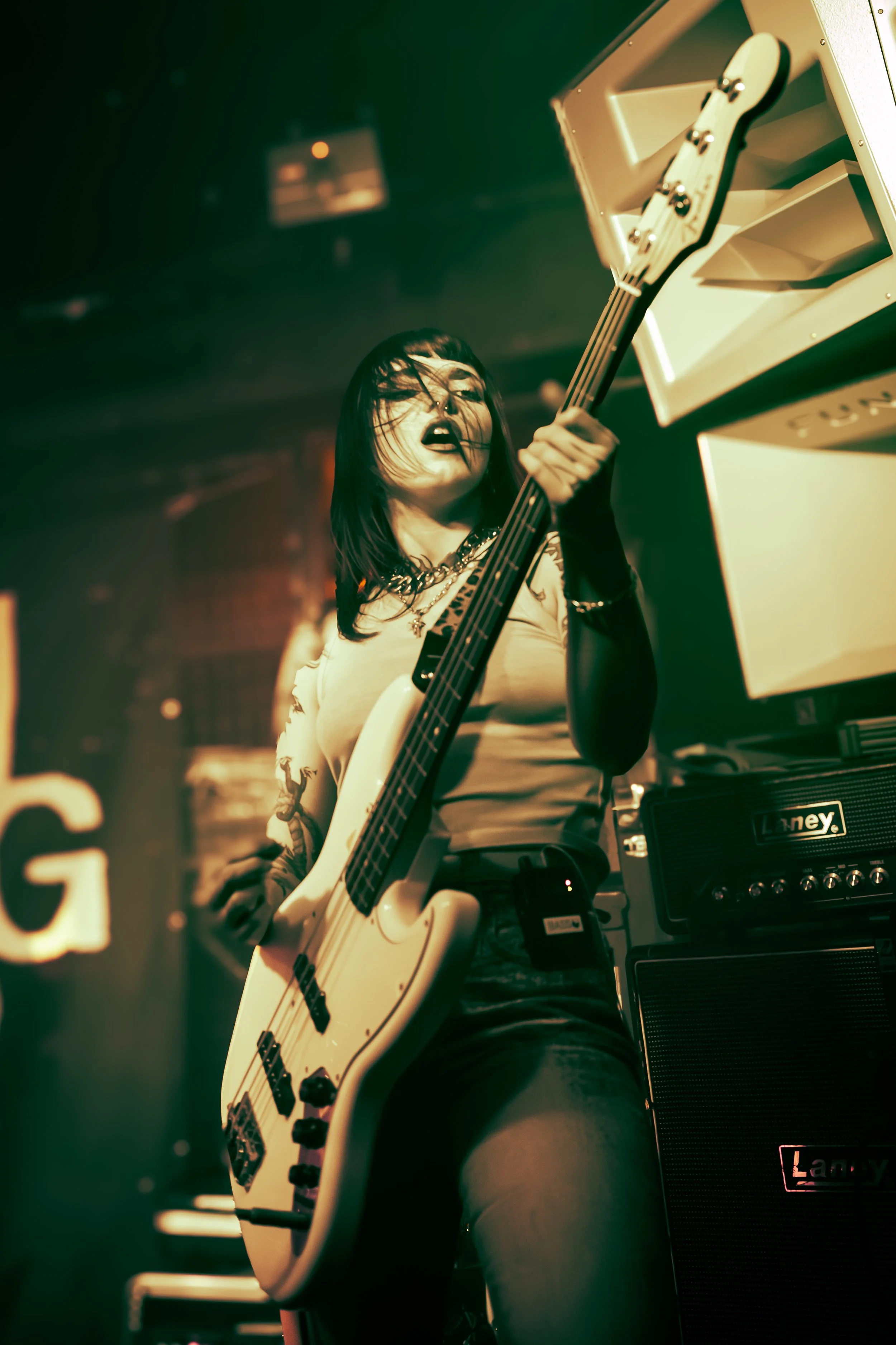 Female musician with tattoos playing white electric guitar in a music studio with amplifier and speaker.